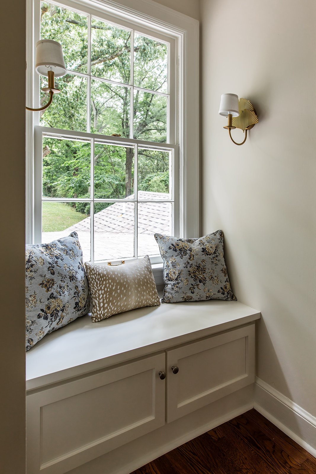 Built-in window seat layered with floral and antelope pillows under a brass sconce