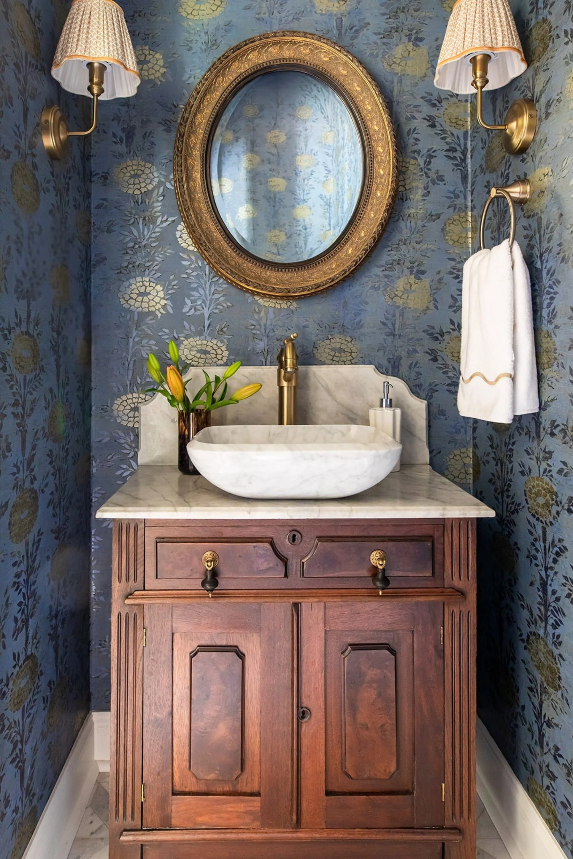 Ornate gold mirror and pleated sconces over a marble vessel sink