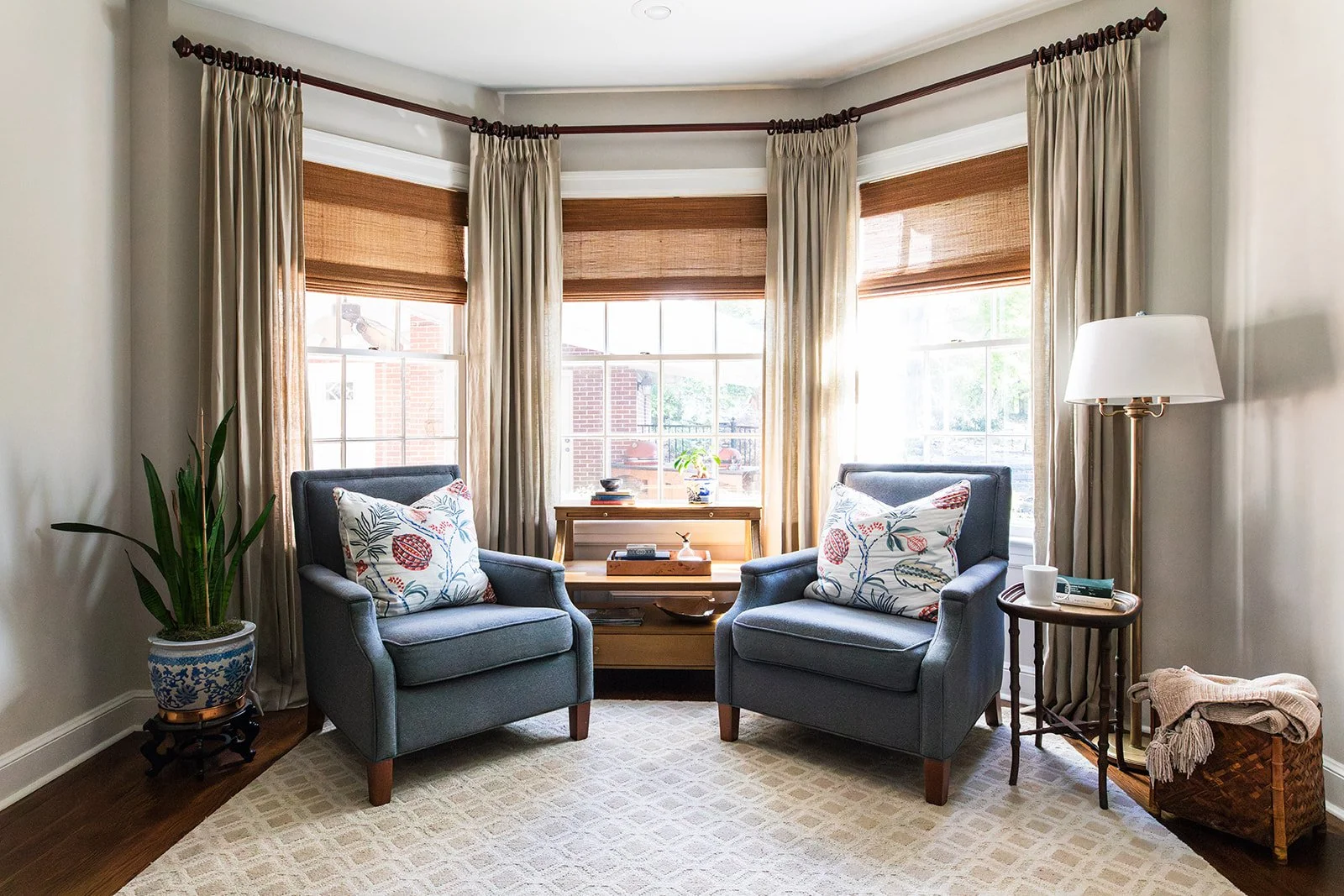 Living room bay window with two blue chairs, woven shades, and a soft rug