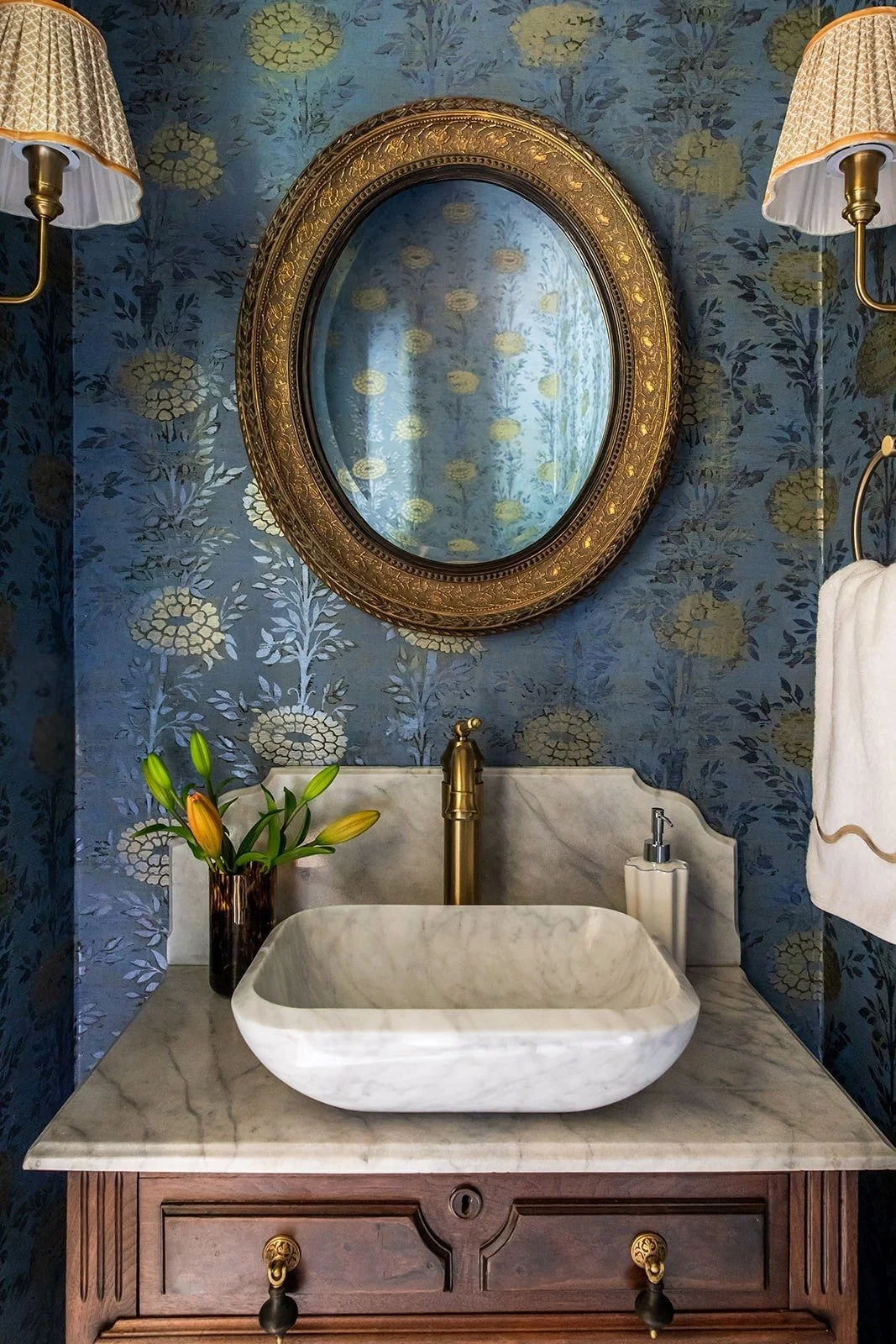 Moody powder room with a gilded mirror, pleated sconces, and antique vanity