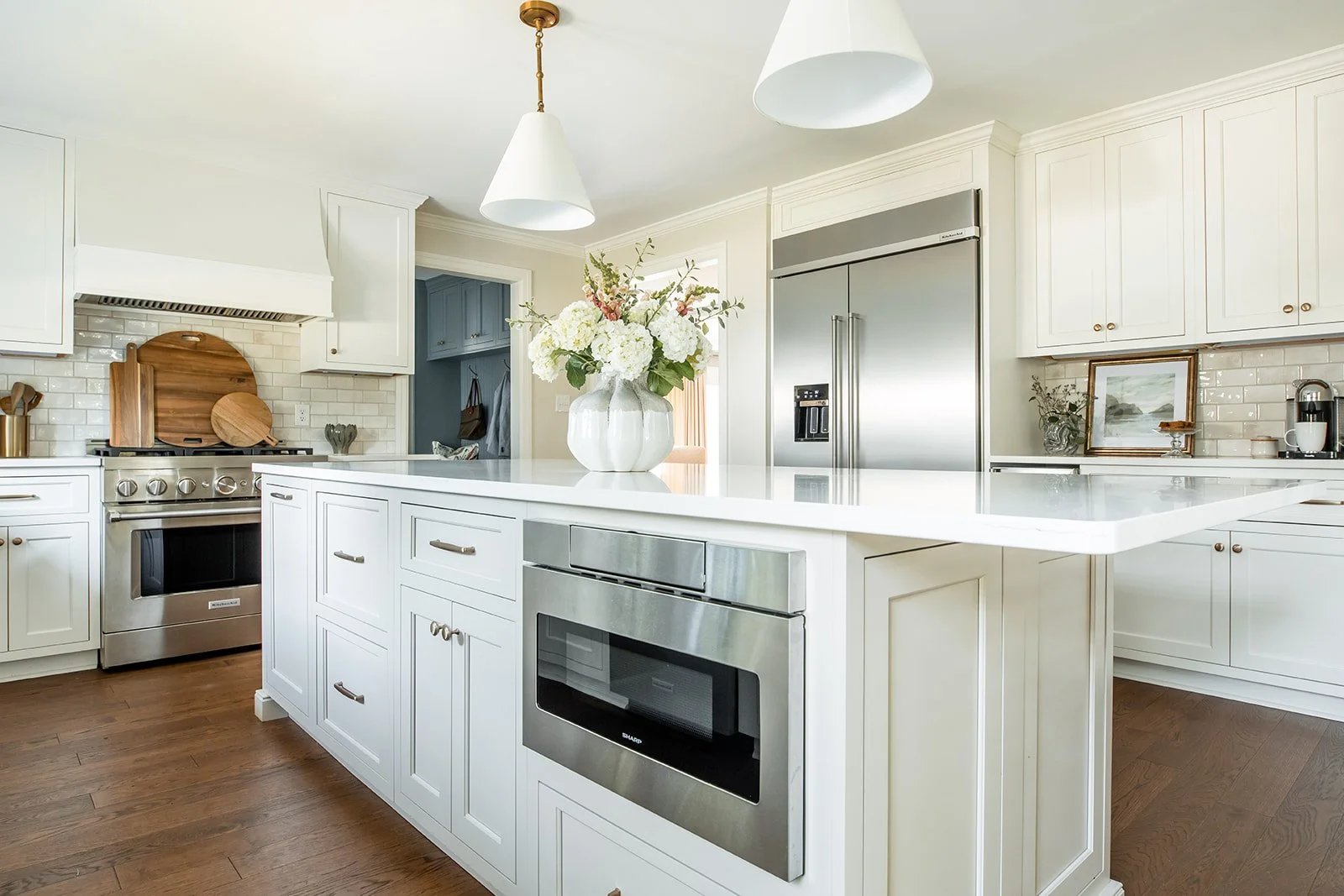 Wide white kitchen with a greige island, custom hood, and stainless range
