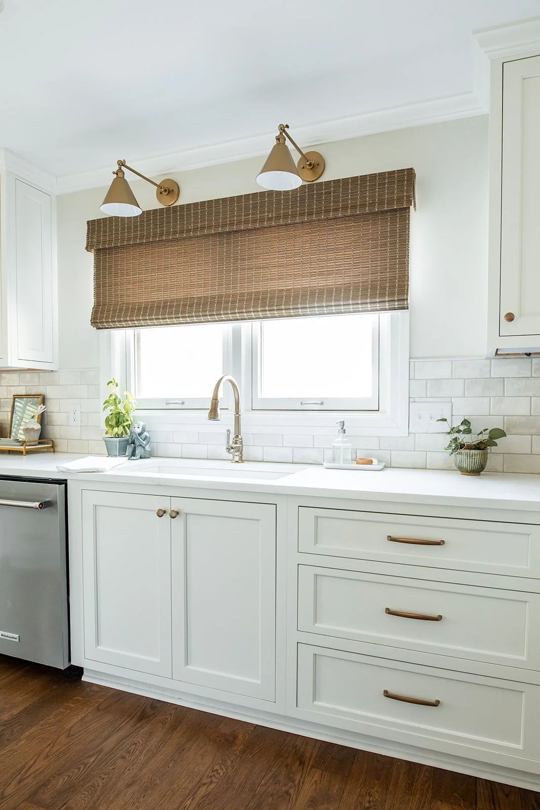 White kitchen sink and dishwasher wall with a brass sconce