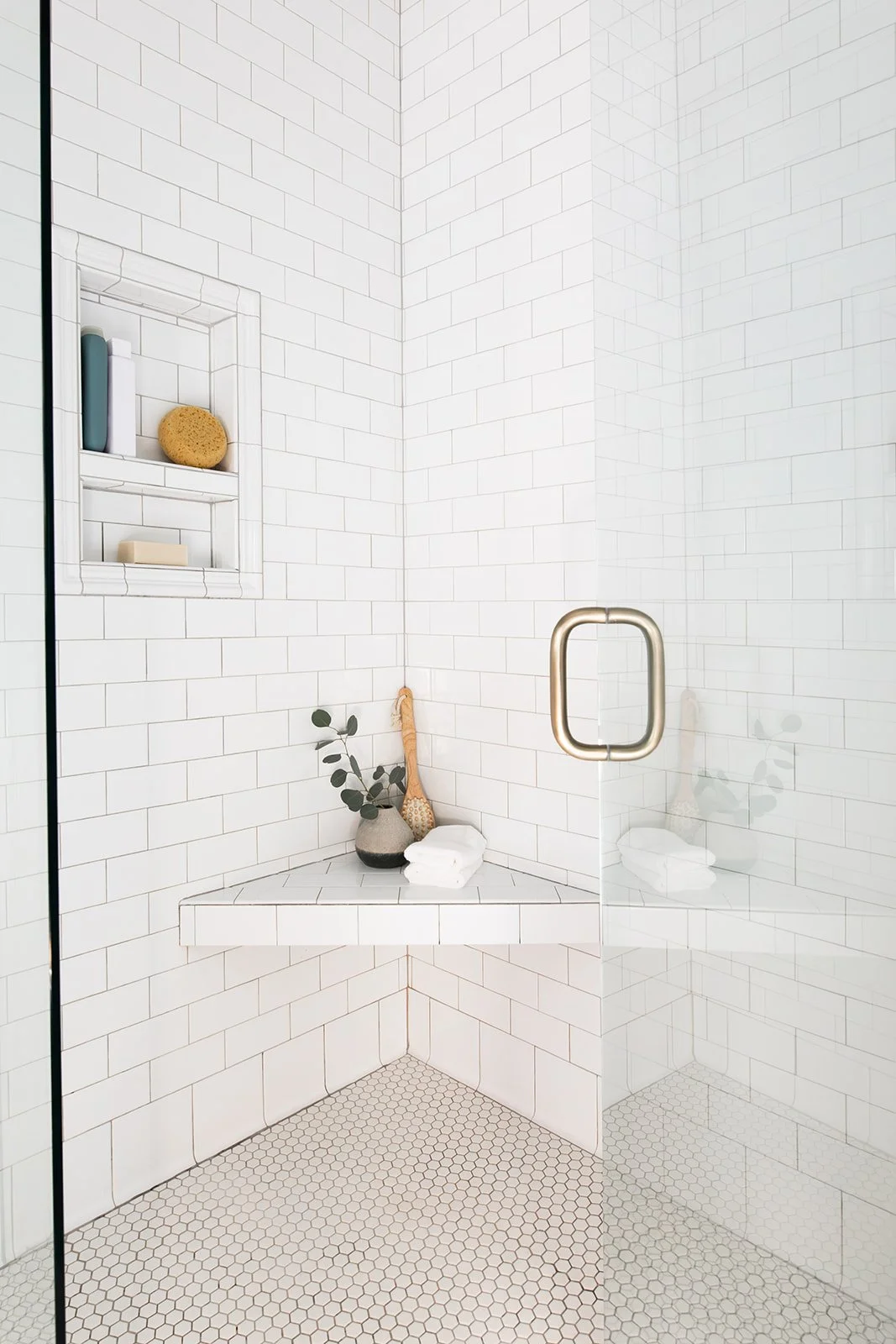 Walk-in shower detail with subway tile, a niche, and a brass hook