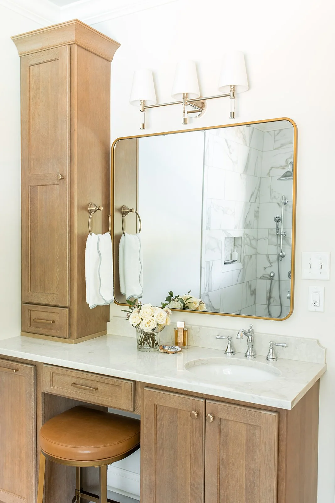 Wood vanity with a linen tower, stool, and brass mirror in the primary bath