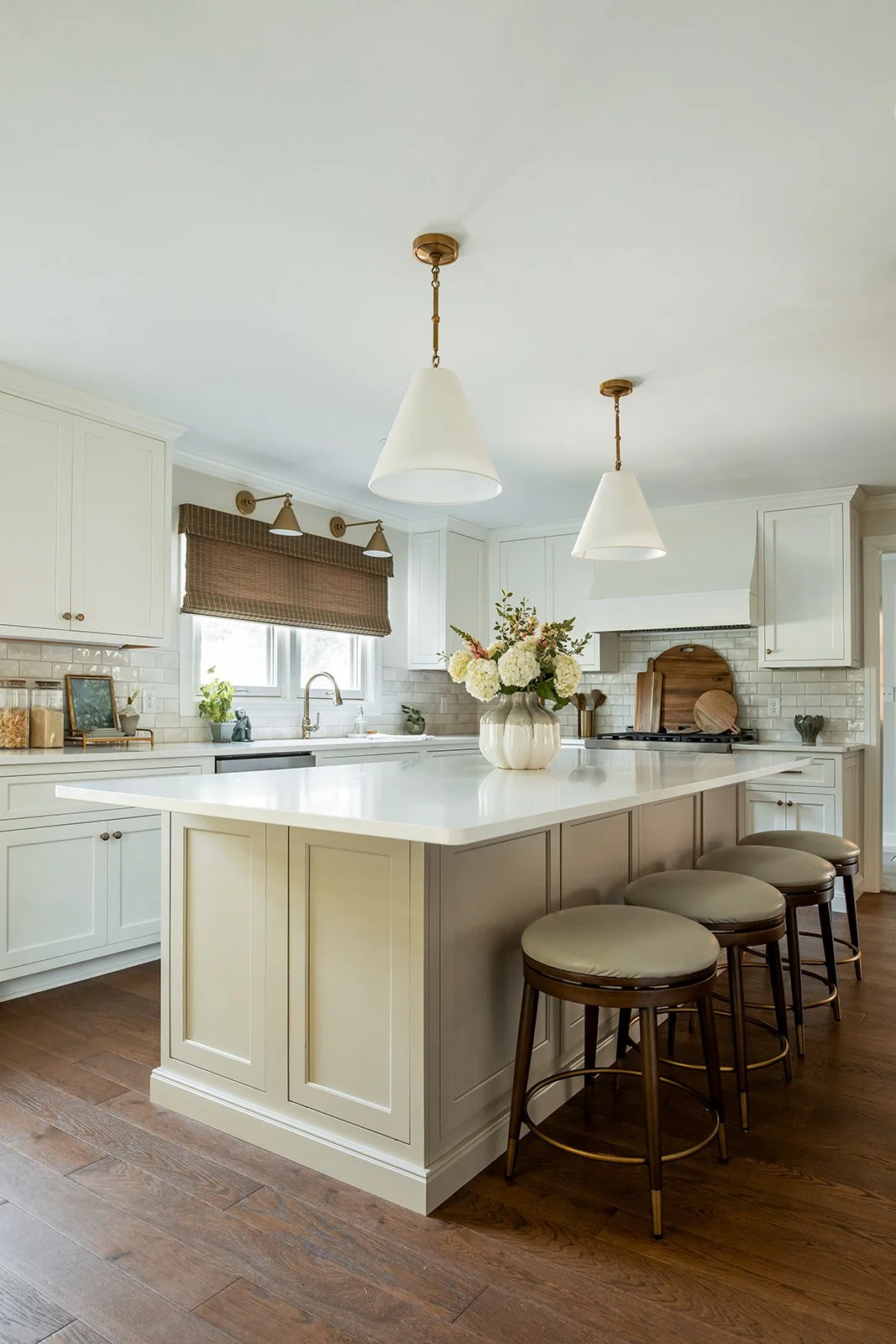White kitchen island with woven barstools and brass shade pendants