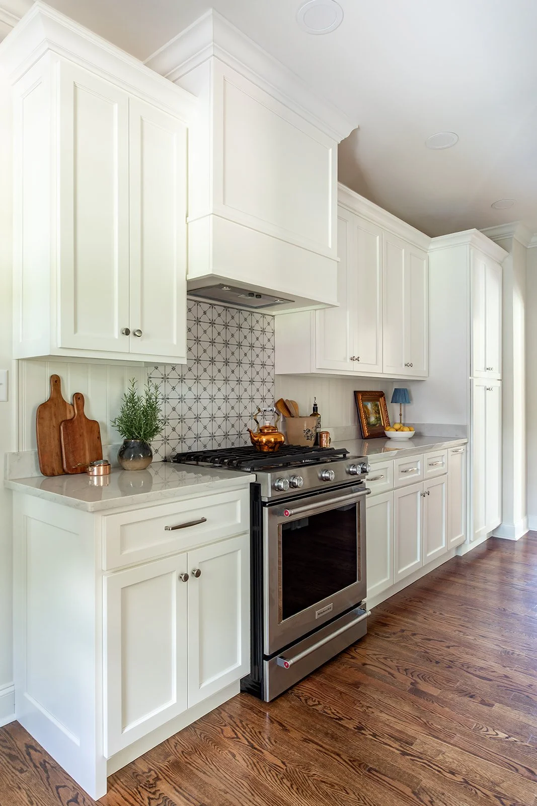 Warm white kitchen with a custom vent hood and restored hardwood floors