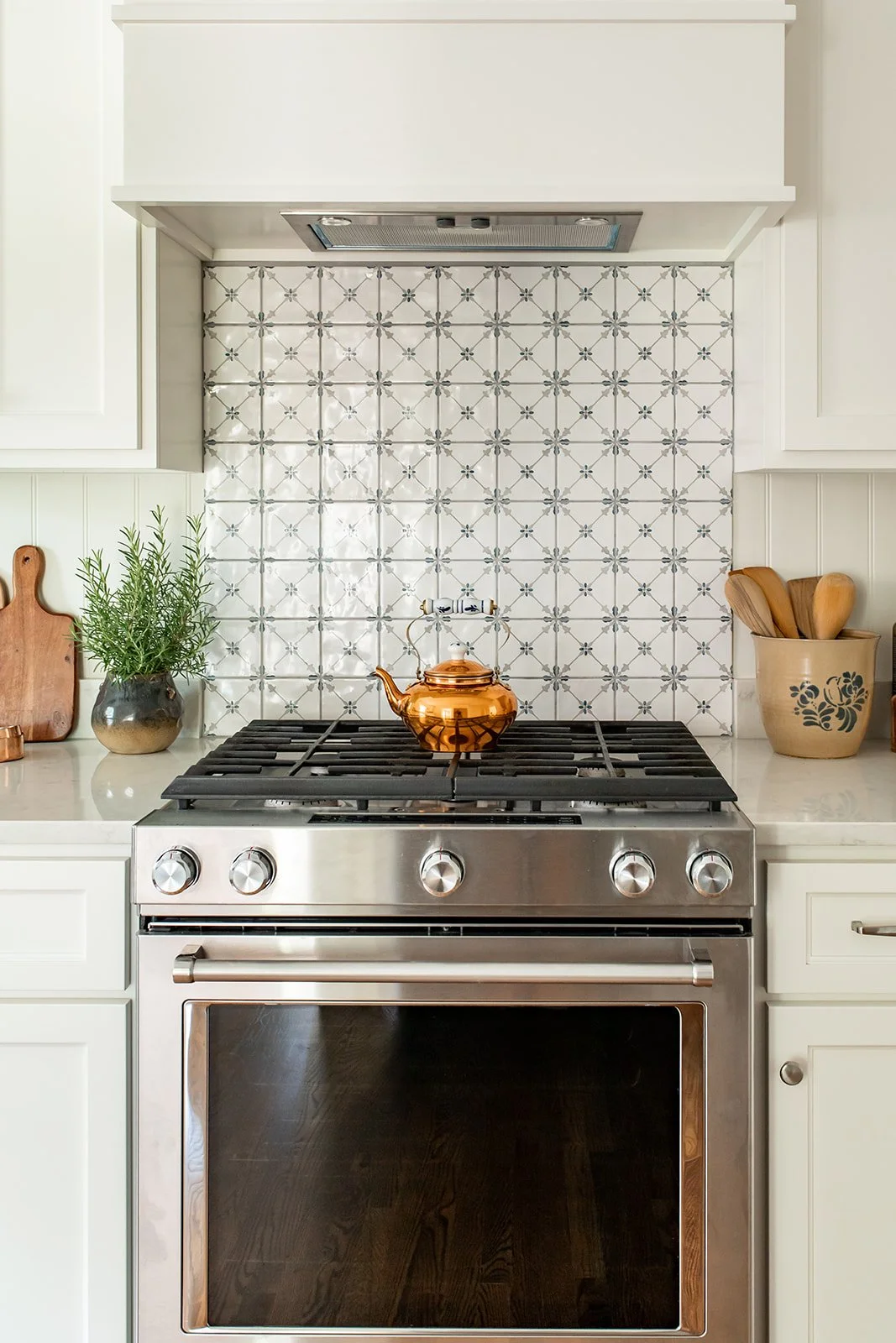 Stainless range with a copper kettle and a patterned tile wall