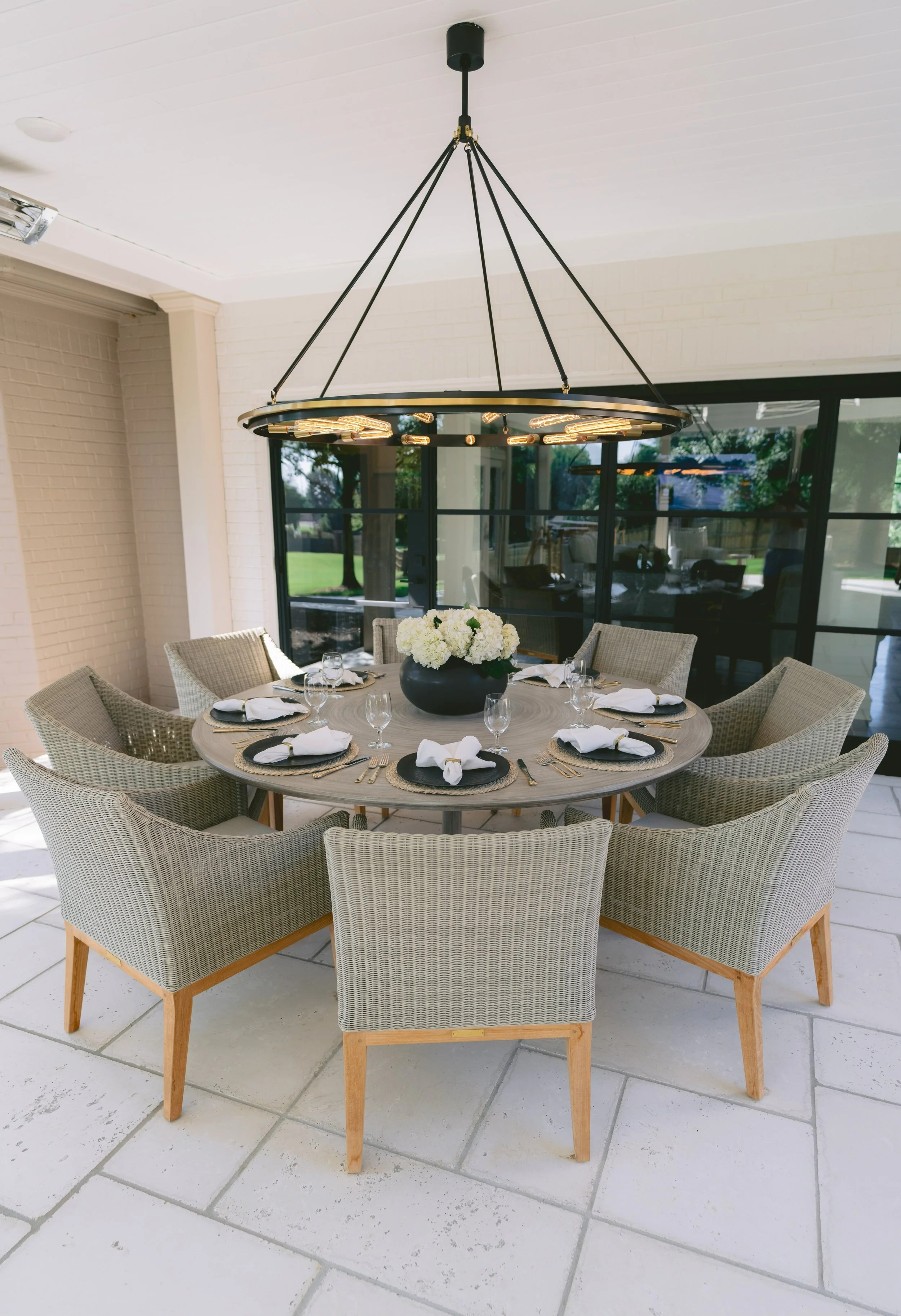 Covered outdoor dining area with a round table, woven armchairs, and a ring chandelier