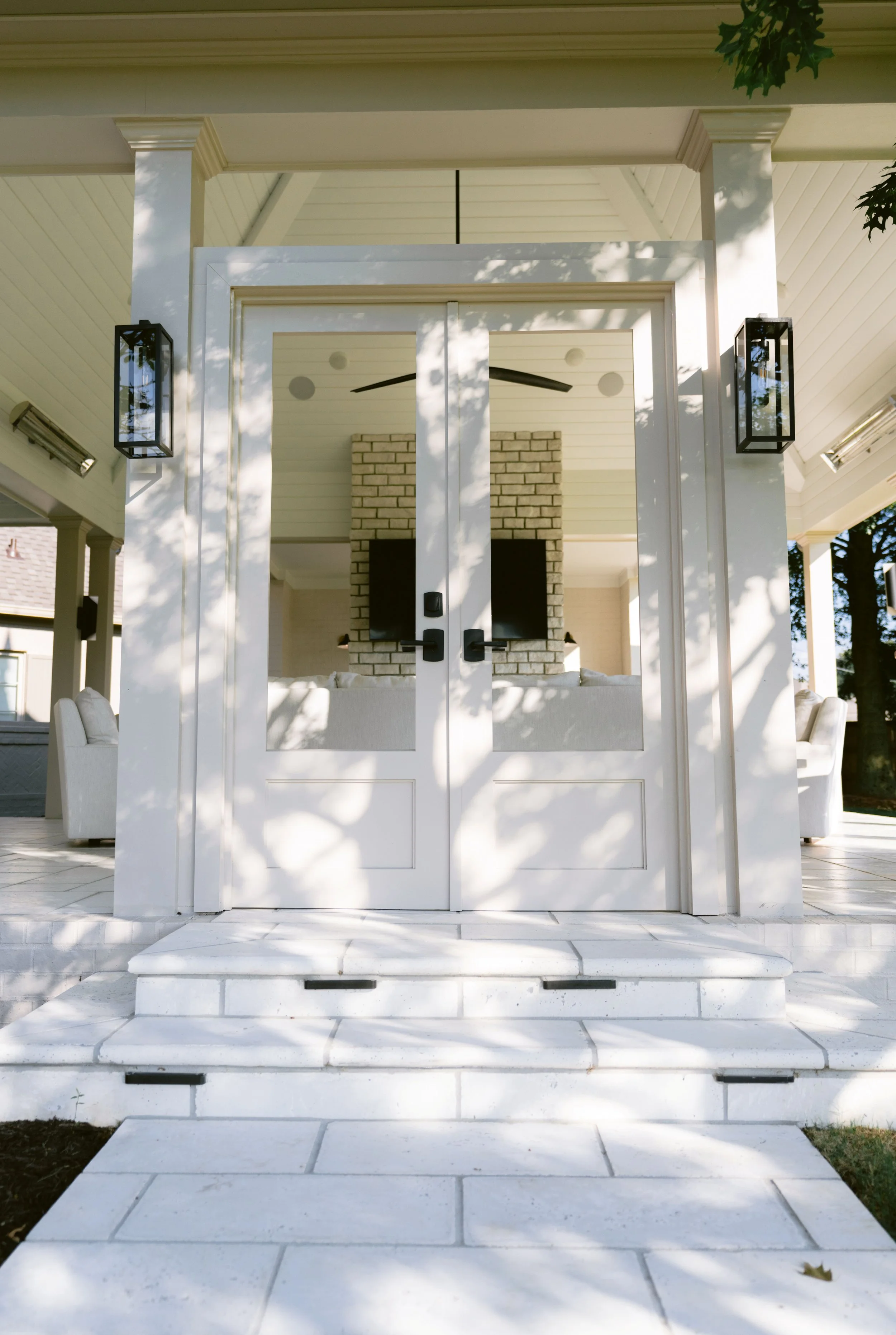Covered porch entry with columns, lanterns, and stone steps to double doors