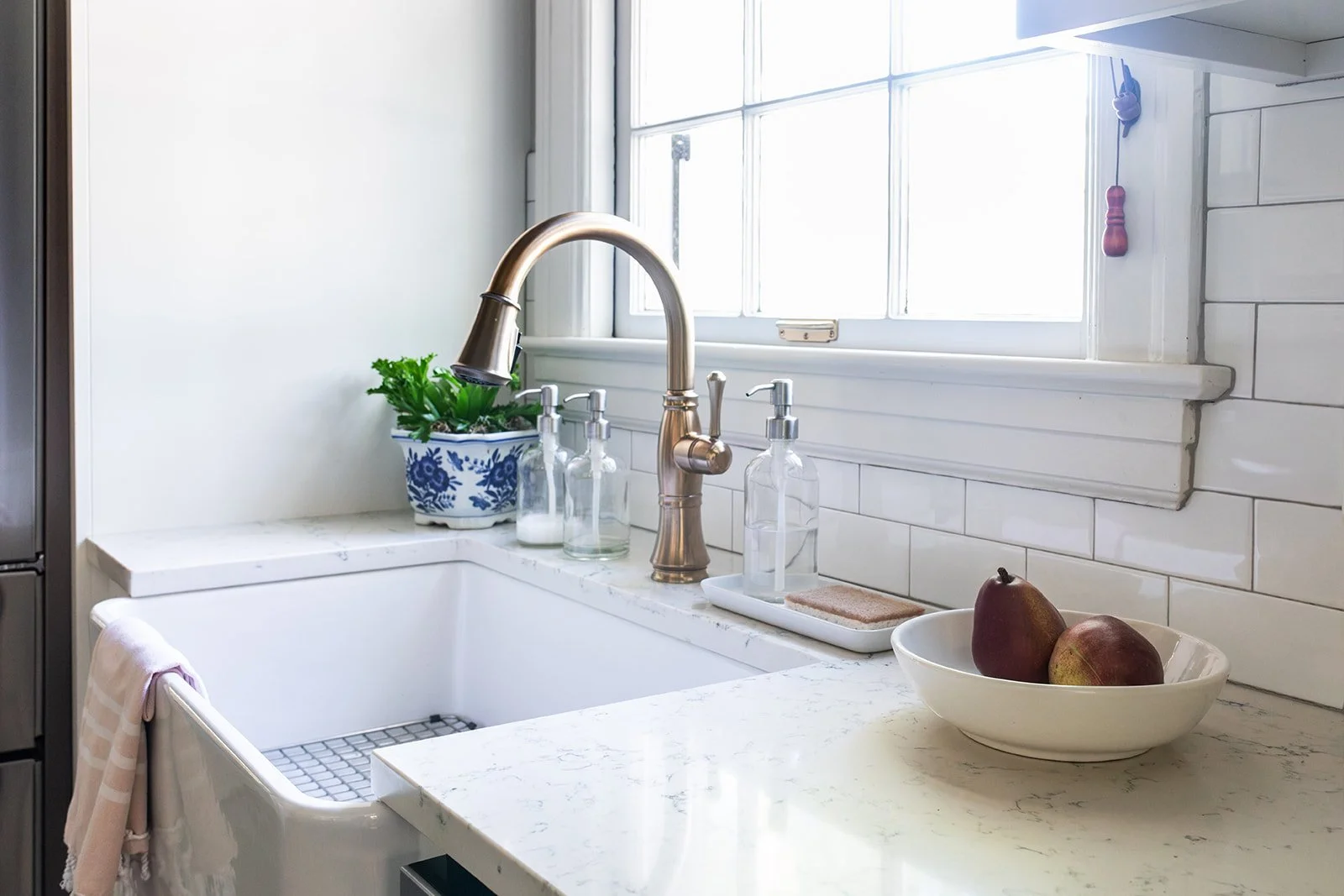 Farmhouse apron sink with a brass faucet beneath a subway-tiled window wall