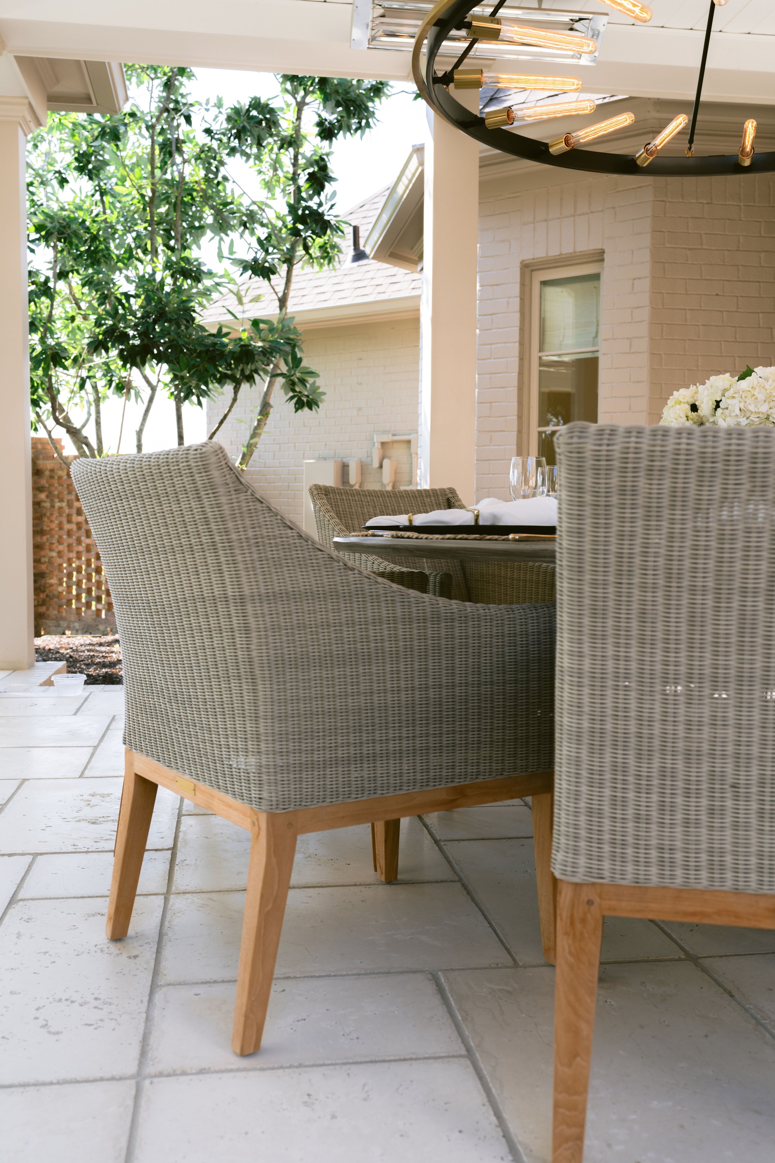 Woven outdoor dining chairs on a stone patio with tree-lined views
