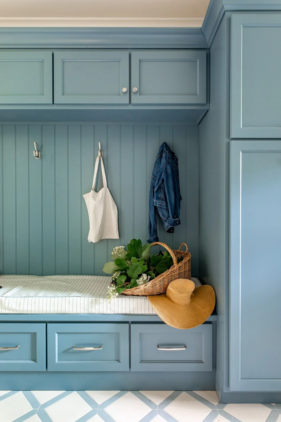 Blue mudroom bench with hooks, drawers, and a checkered tile floor