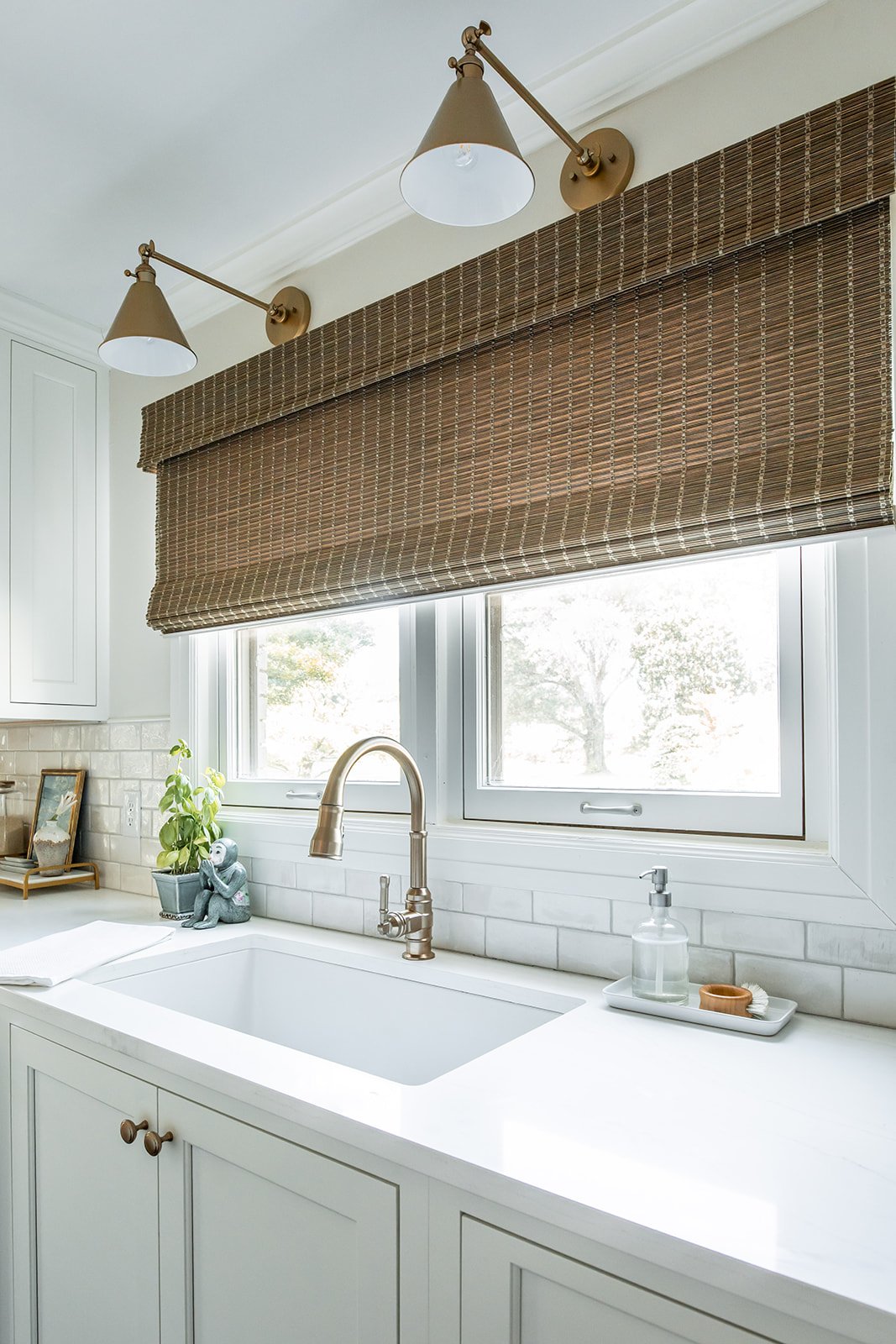 Large sink beneath a window with a brass swing-arm sconce and woven shade