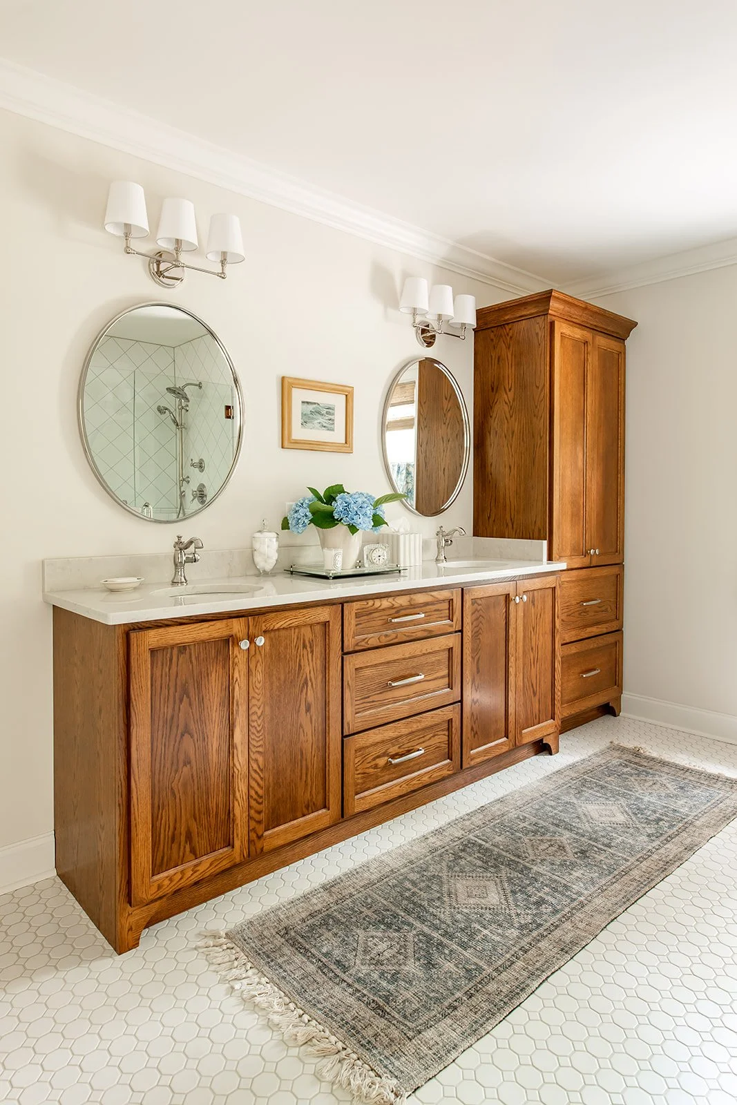 Master bath with a custom wood double vanity, linen tower, and round mirrors