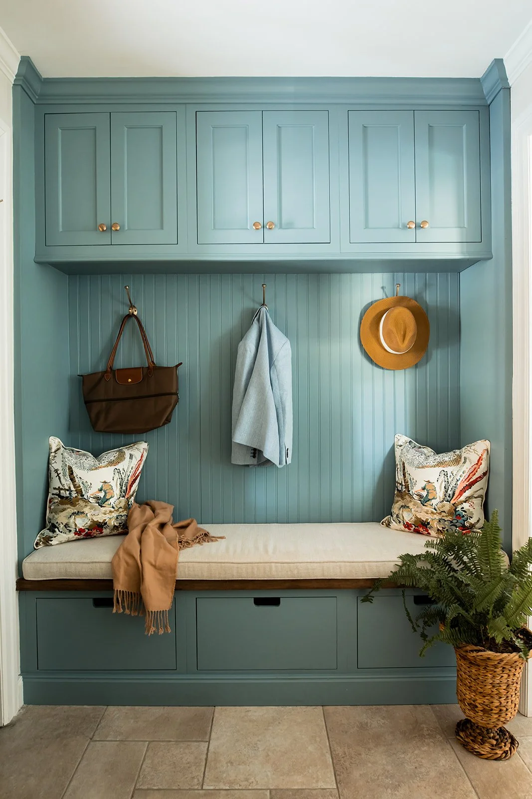 Teal beadboard mudroom bench with hooks, a hat, and floral pillows