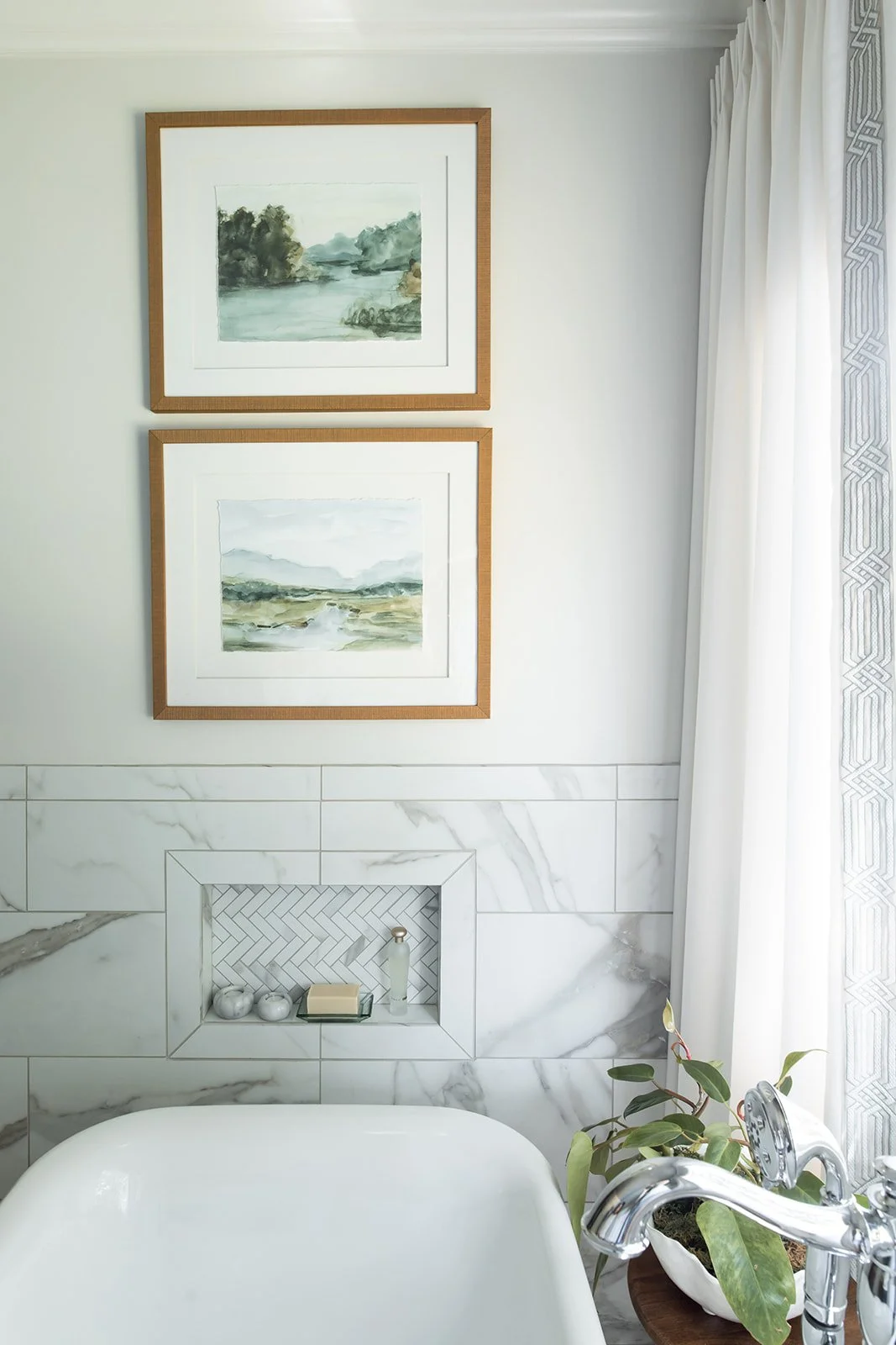 Framed landscape art beside the cast stone tub and marble-look wall