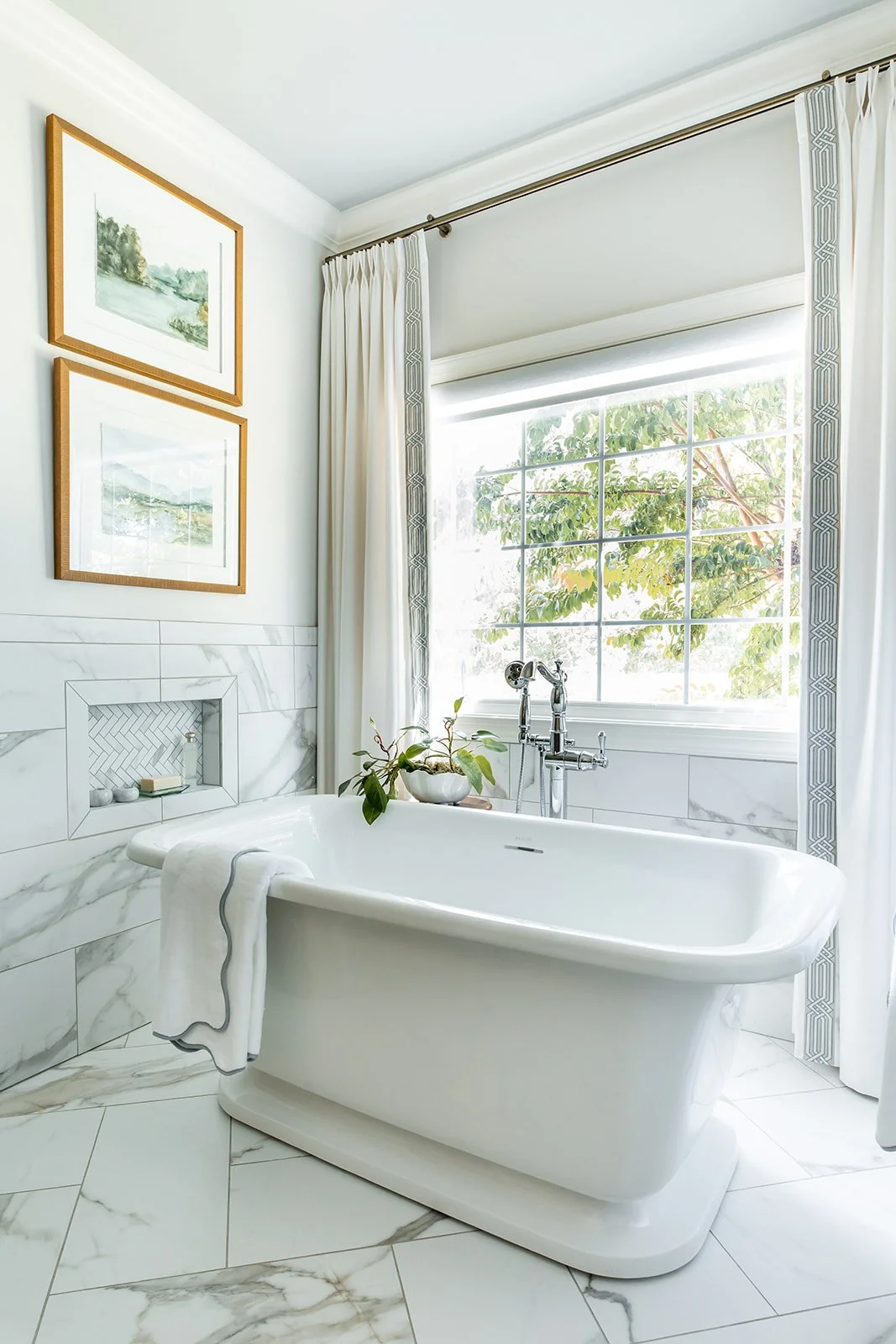 Cast stone soaking tub beneath a window with a marble-look floor and greenery