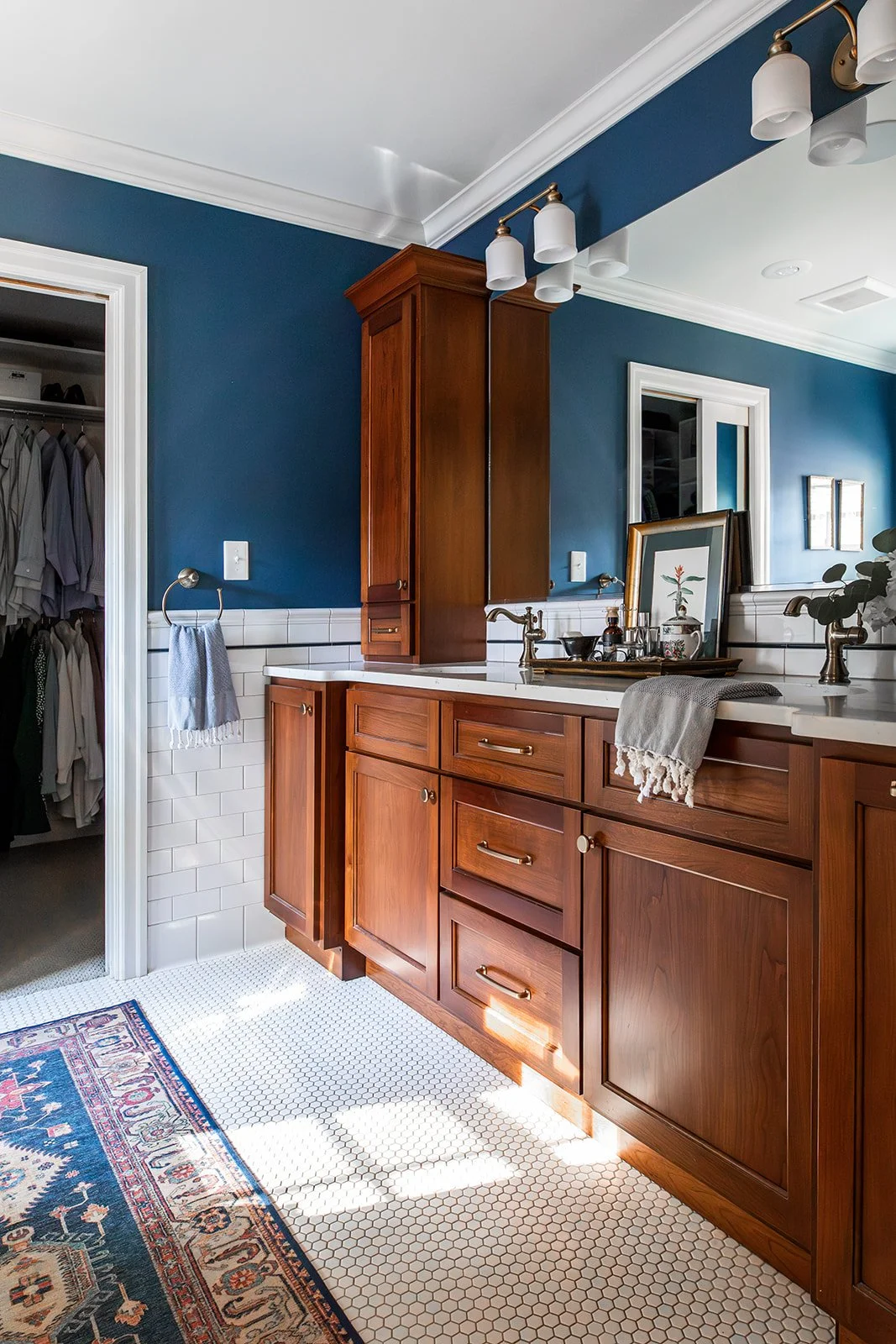 Cherry vanity with a mirror and sconces framed by navy walls and subway tile