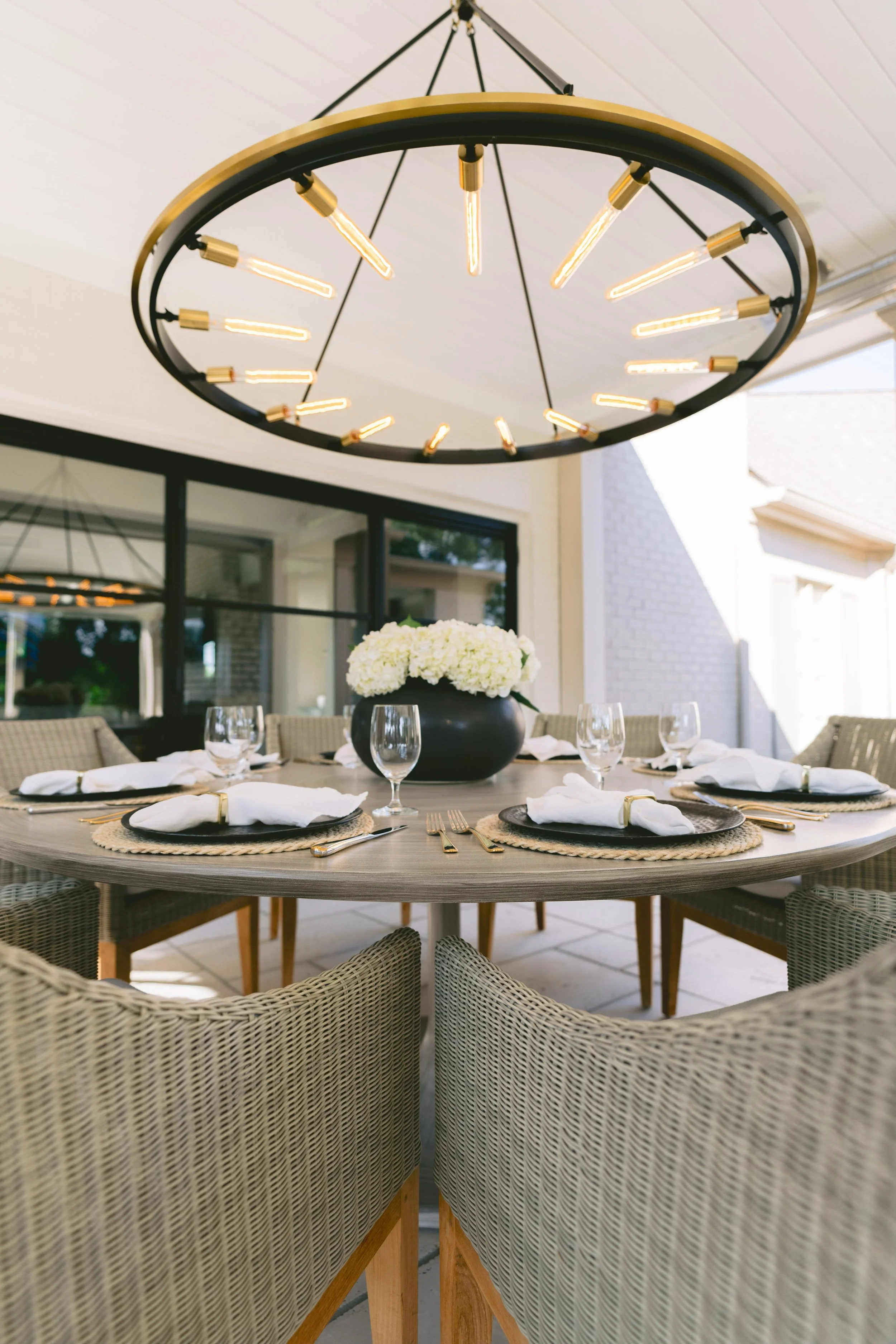 Outdoor dining table set beneath a black-and-brass ring chandelier with hydrangeas
