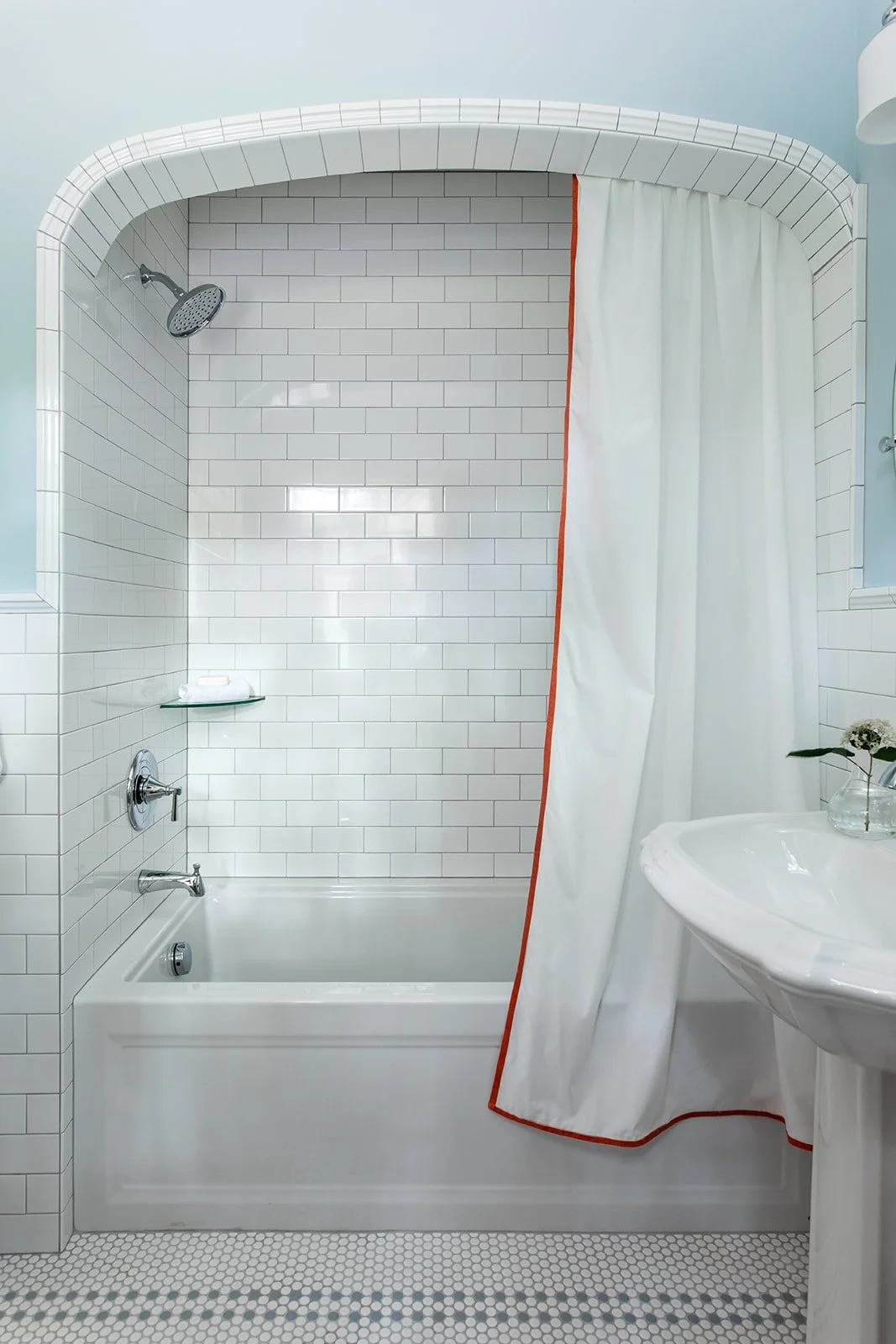 Arched subway-tile tub and shower with a pedestal sink and orange-trimmed curtain