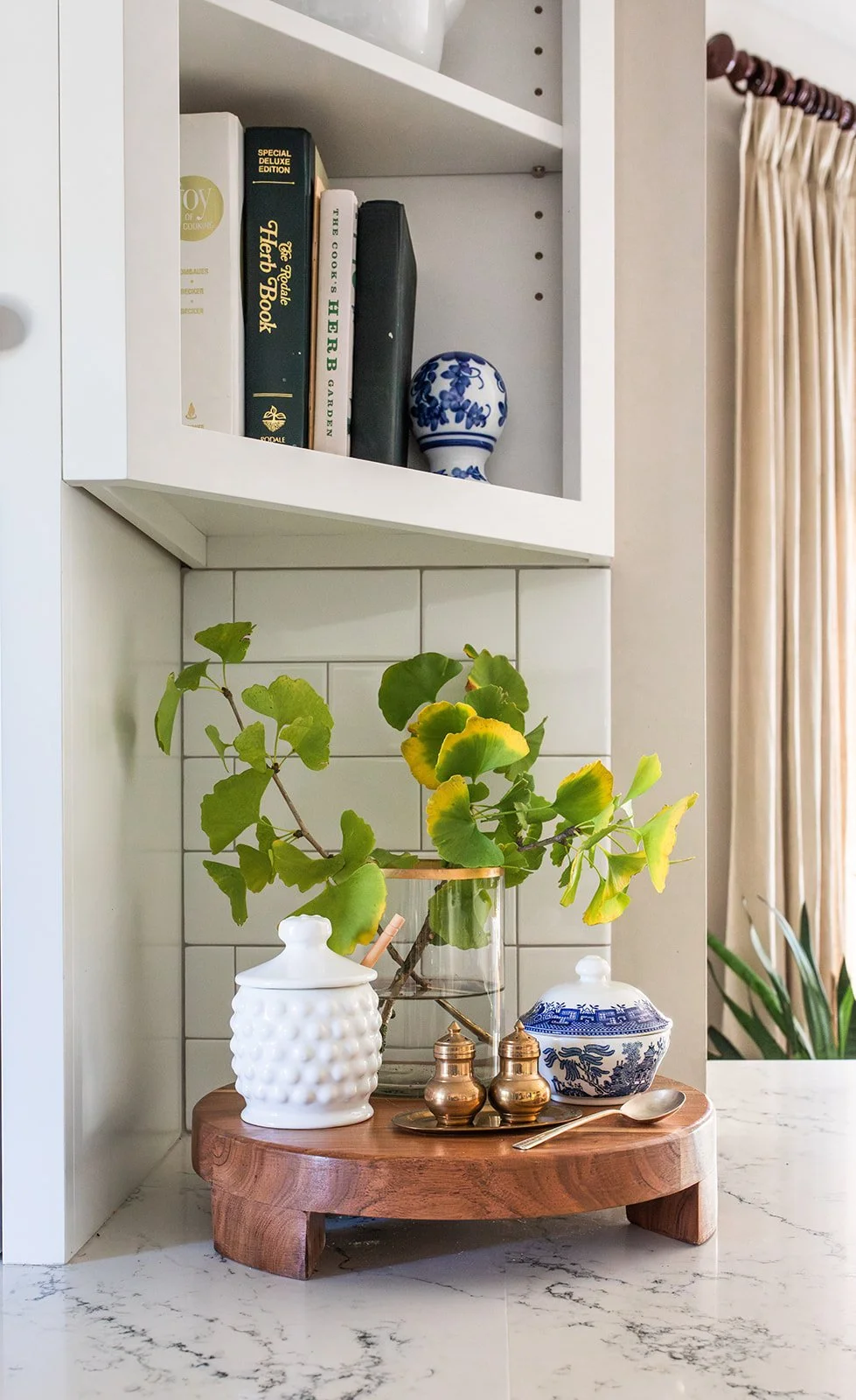 Built-in shelf styled with books, a ginger jar, and greenery beside linen drapery