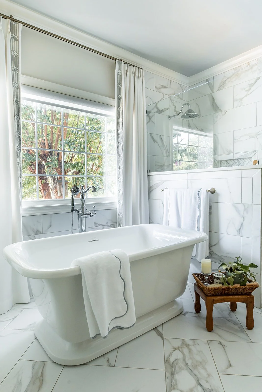 Cast stone soaking tub with a floor-mounted filler and a tree-lined window view