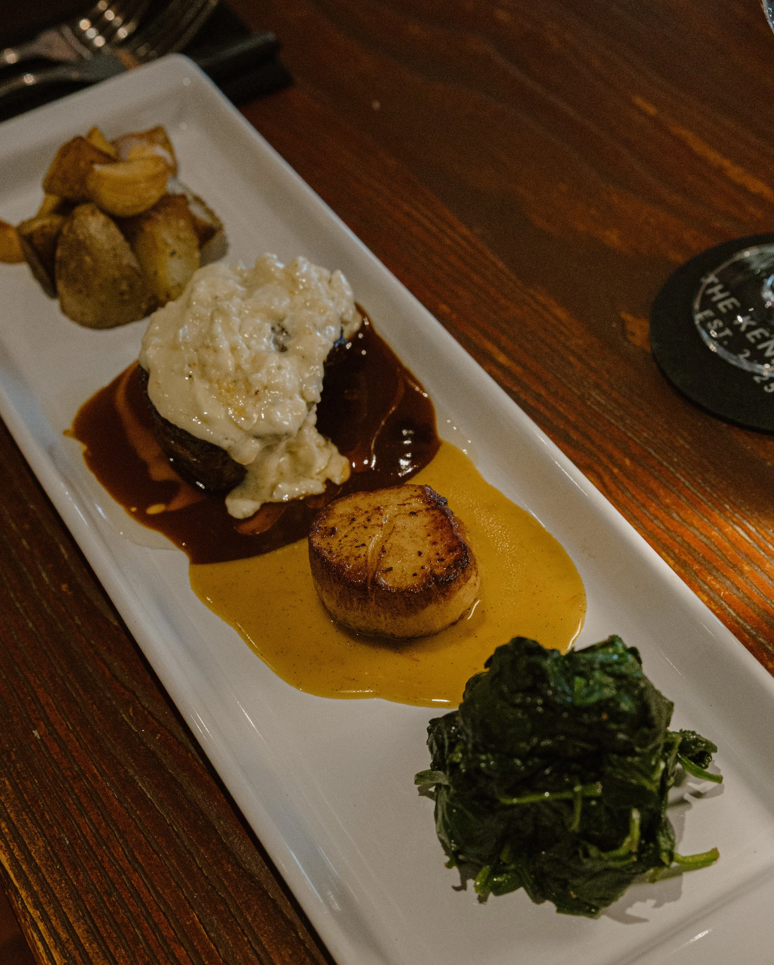 Steak and Scallop topped with Maytag blue cheese, port demi glaze, seared scallop, saffron vanilla bean beurre blanc, Served with duck fat roasted Yukon Gold potatoes & pancetta wilted spinach