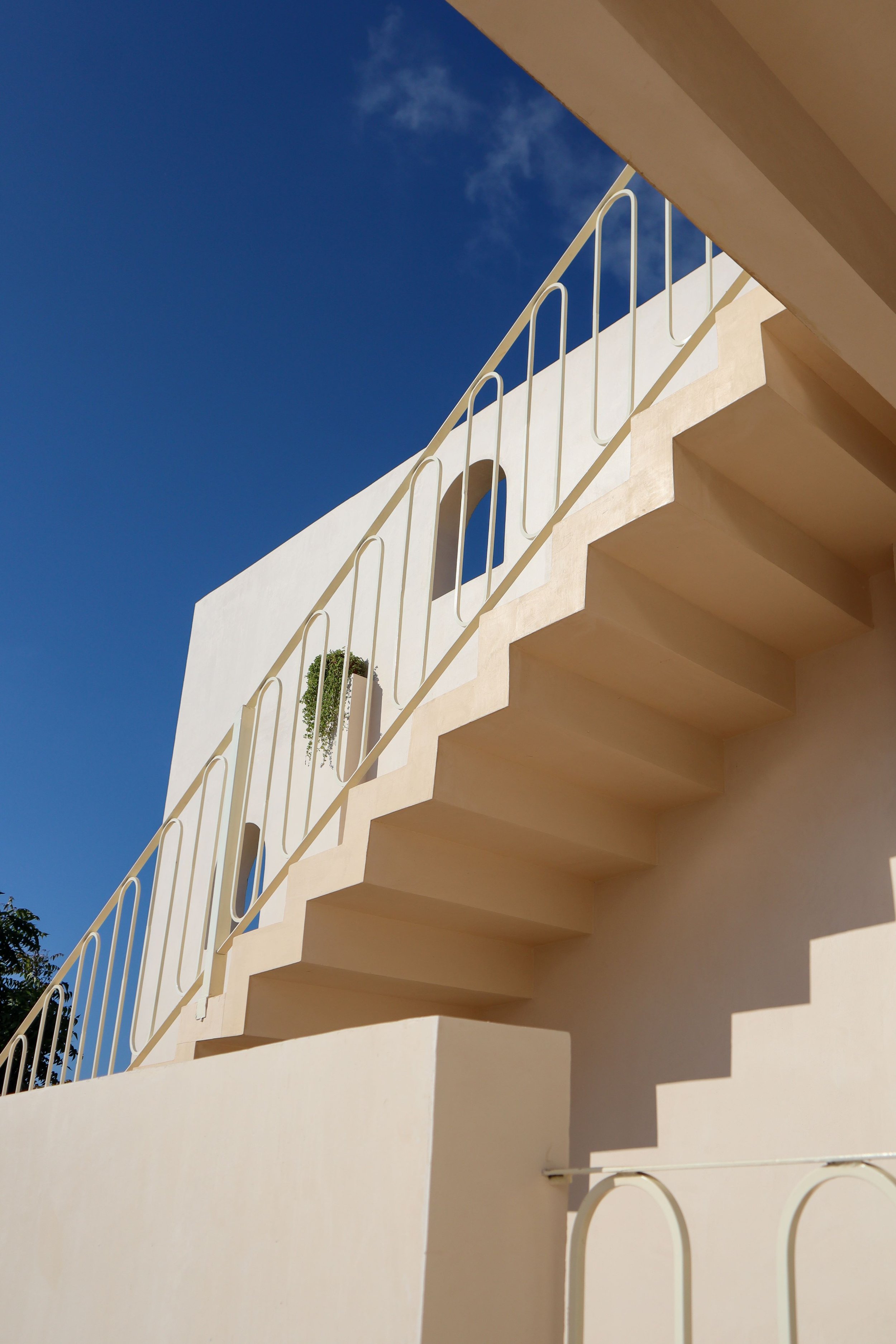 Minimalist architectural staircase with cream-colored steps and railings against a clear blue sky.