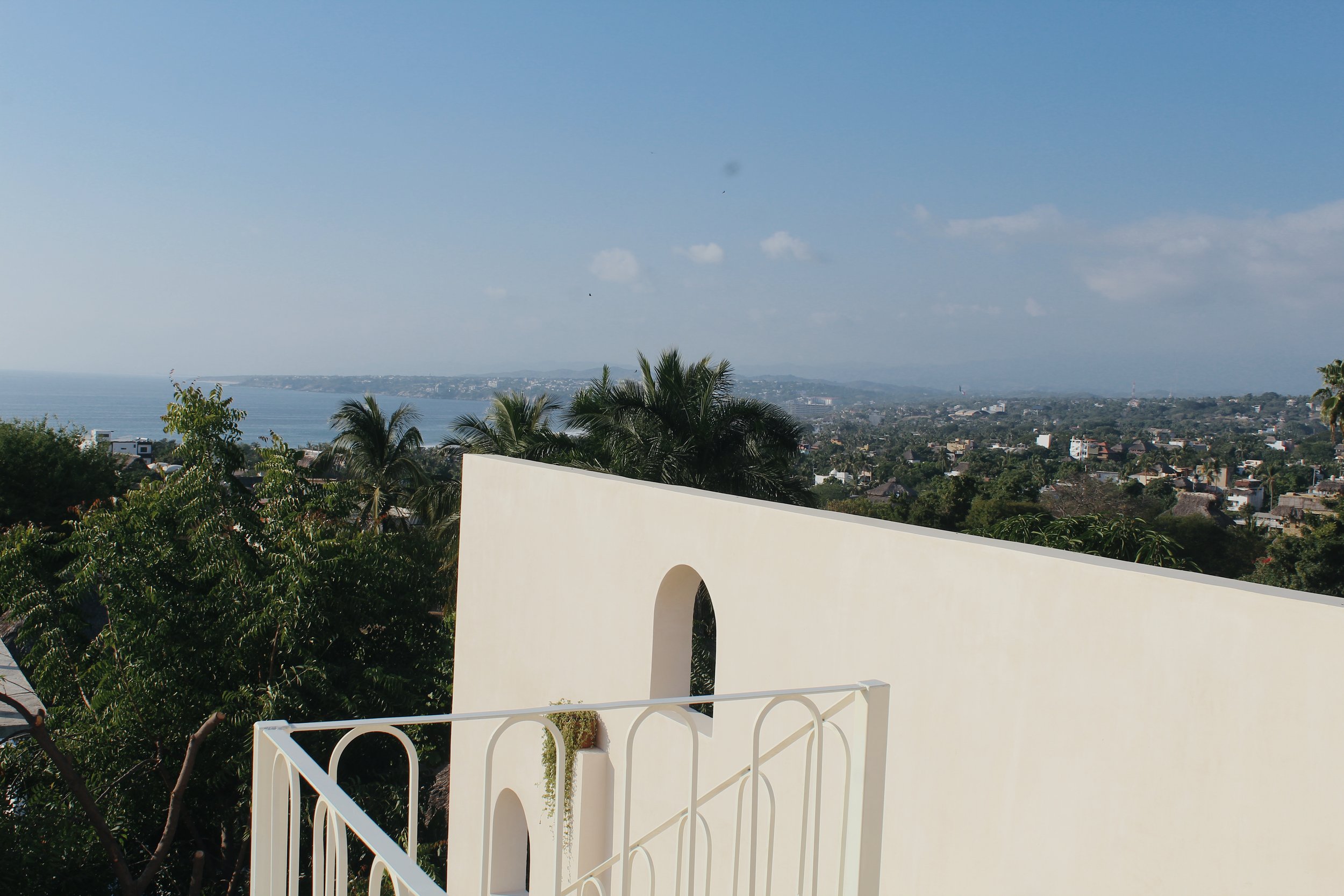 Scenic view from a rooftop terrace with sea in the distance, palm trees, and a clear blue sky.