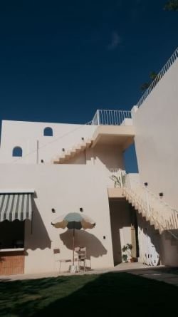 Exterior view of a white building with stairs, flat roof, and umbrella on a sunny day.