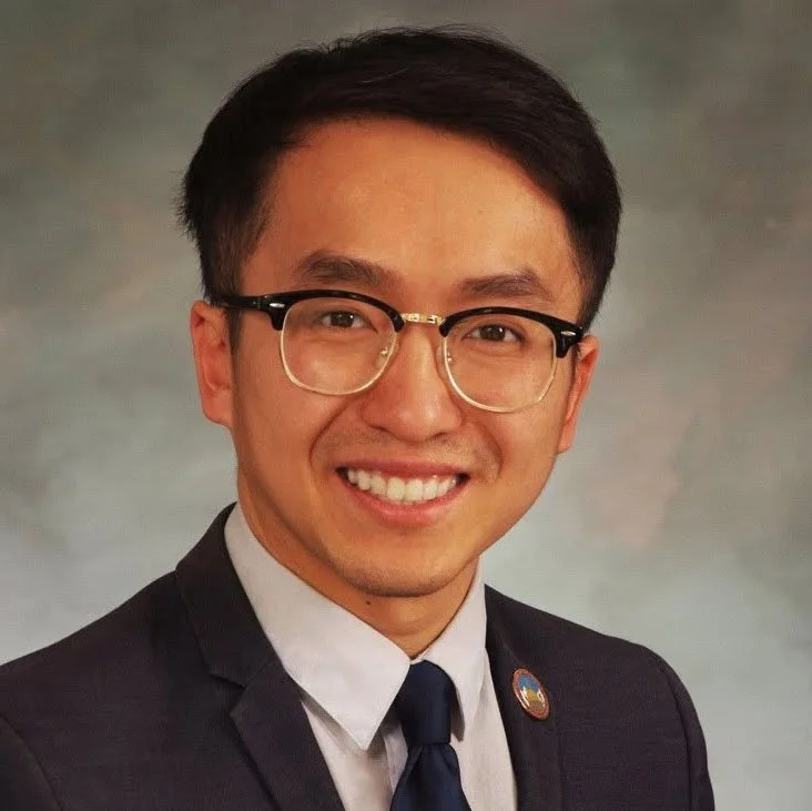 A young man with glasses in a business suit smiling at the camera.