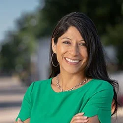 Smiling woman in a green top with dark hair, outdoor background