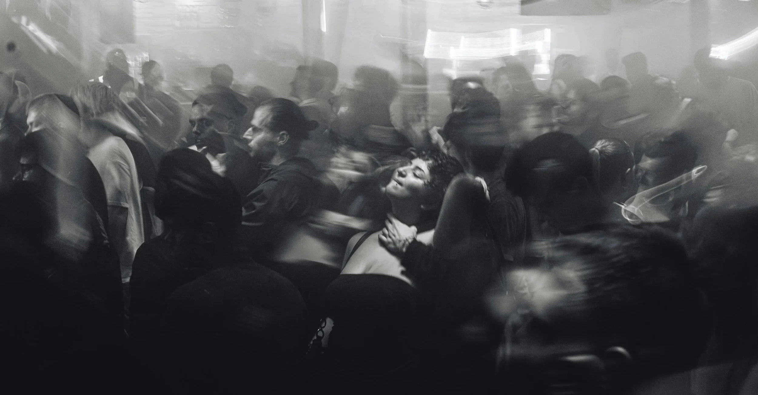 Black and white photo of a crowded bus or train with many passengers seated and standing, with some blurred motion.
