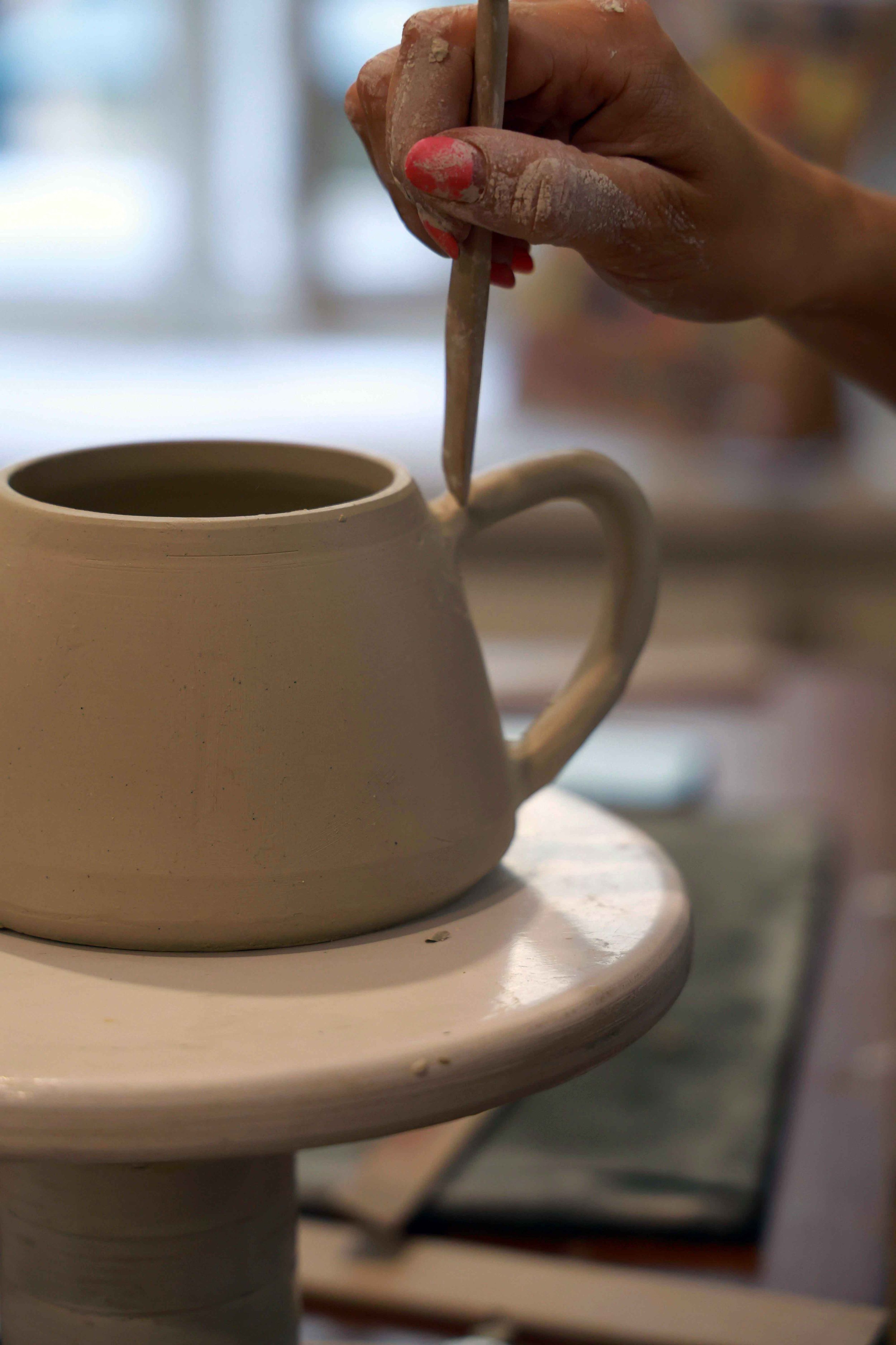 Female hands shaping a clay mug on a pottery wheel, carefully crafting the piece with attention to detail in a creative and artistic workspace.