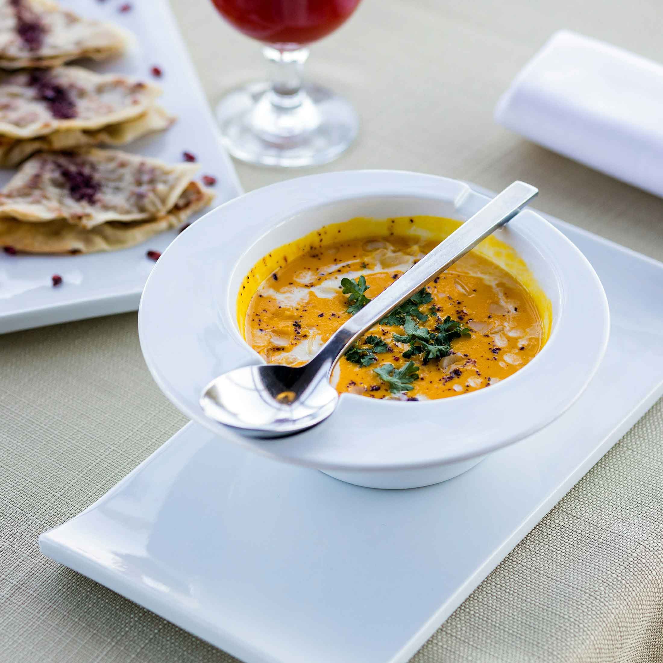Close-up of pumpkin soup on a table, served outdoors with good lighting, showcasing a light and comforting meal in a fresh and vibrant setting.