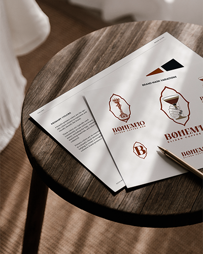 Two pages of a brand guide for a coffee shop displayed on a dark table in a room, with window blinds casting shadows and the shade gently blowing in, creating a dynamic and inviting atmosphere.
