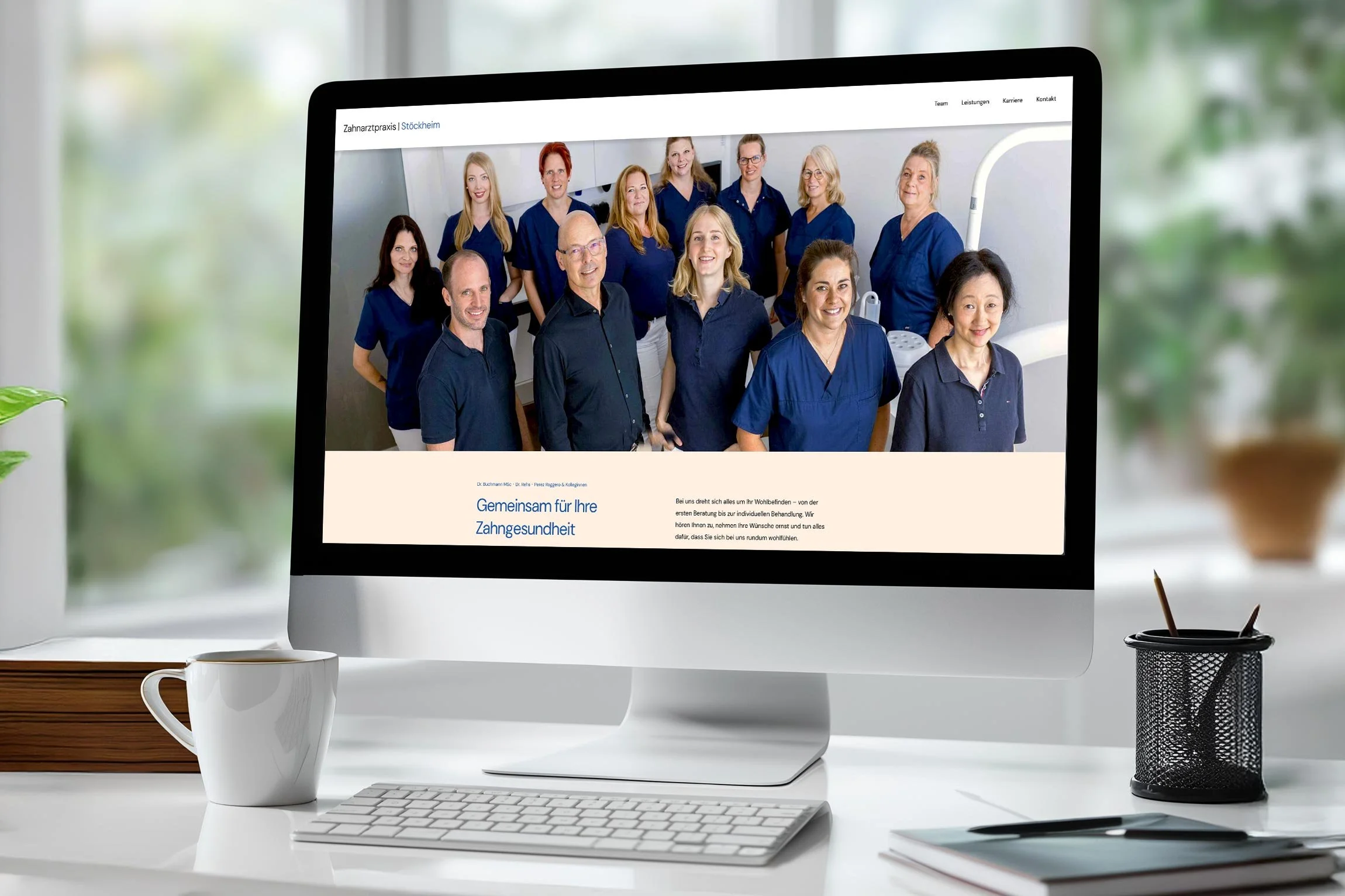 Computerbildschirm zeigt eine Webseite einer Zahnarztpraxis mit einem Team aus Zahnärzten und zahnmedizinischem Personal, alles in blauen Kleidung, vor weißem Hintergrund. Am unteren Bildrand steht Text in Deutsch.