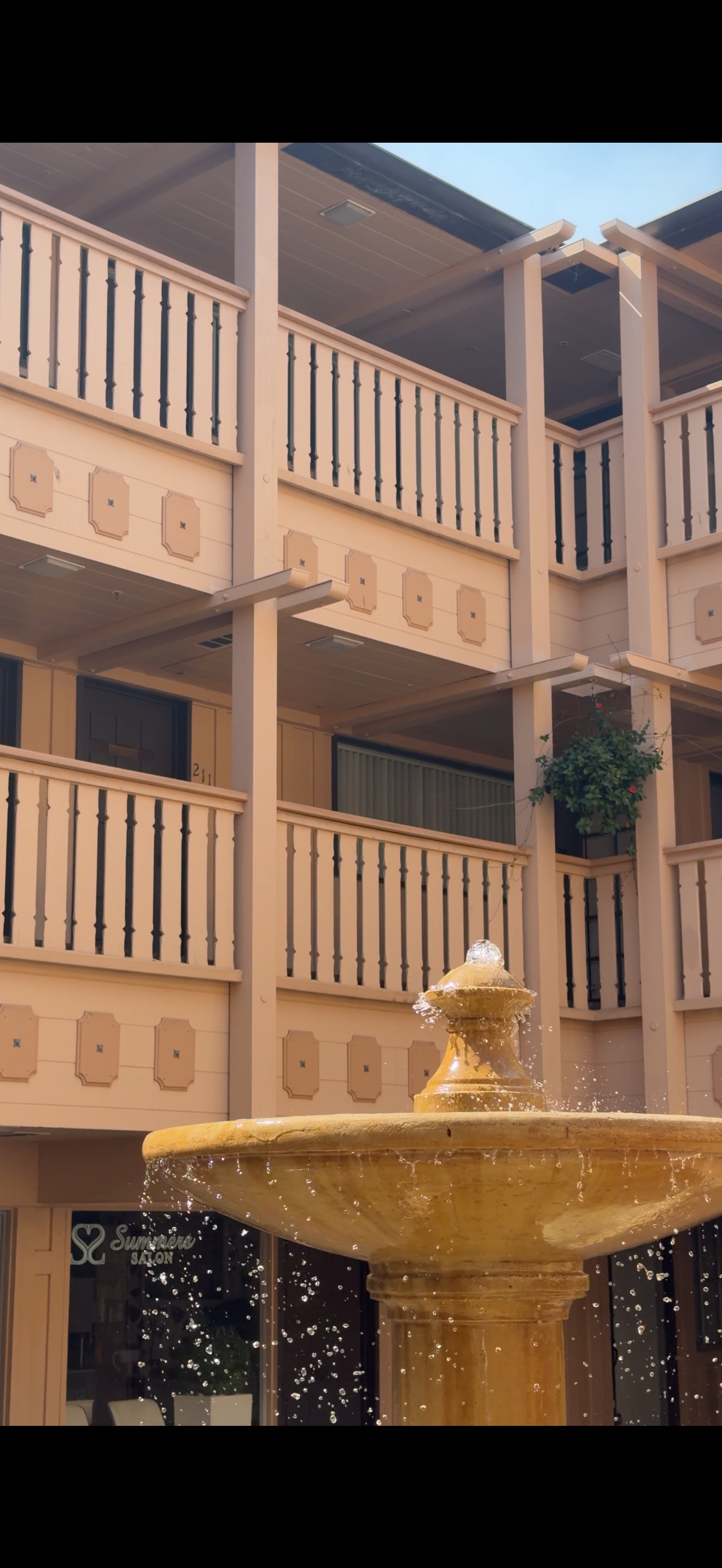 A multi-story building with balconies and railing, and a fountain in the foreground.