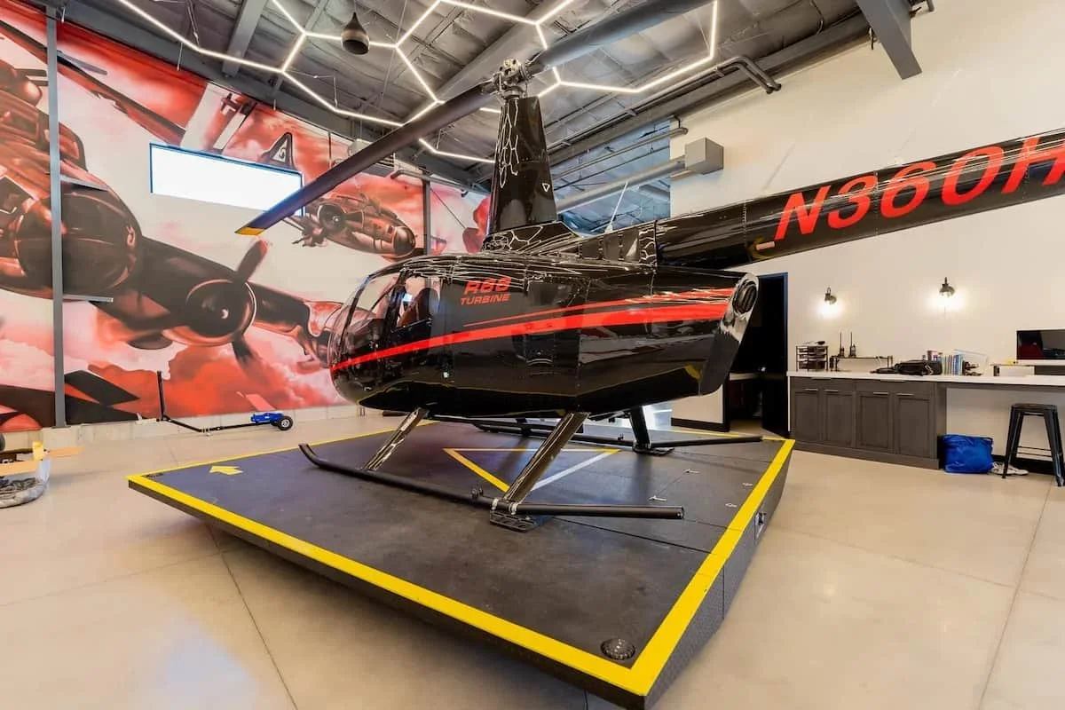 A black helicopter with red stripe and registration number N360H displayed on its tail, inside a room with racing-themed wall art and a work desk.