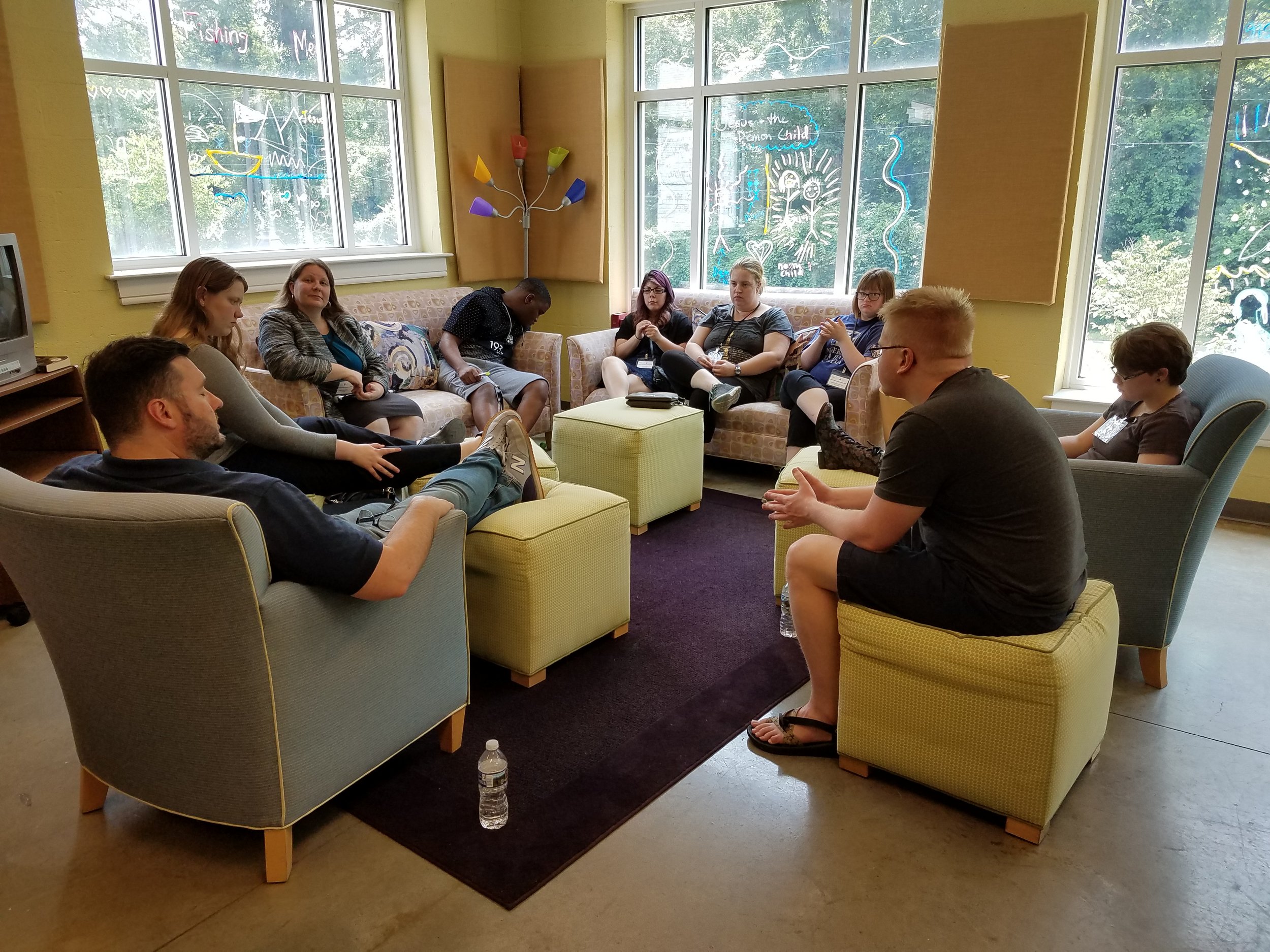A group of young adults sits in a comfortable seating area chatting.