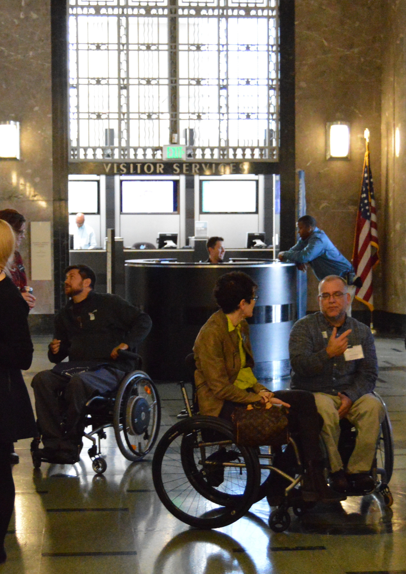 Several folks in wheelchairs talk in front of a visitor services desk
