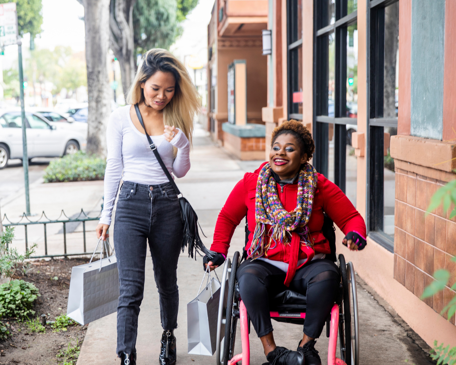 two people at an outdoor shopping center holding bags one is walking the other is using a wheelchair
