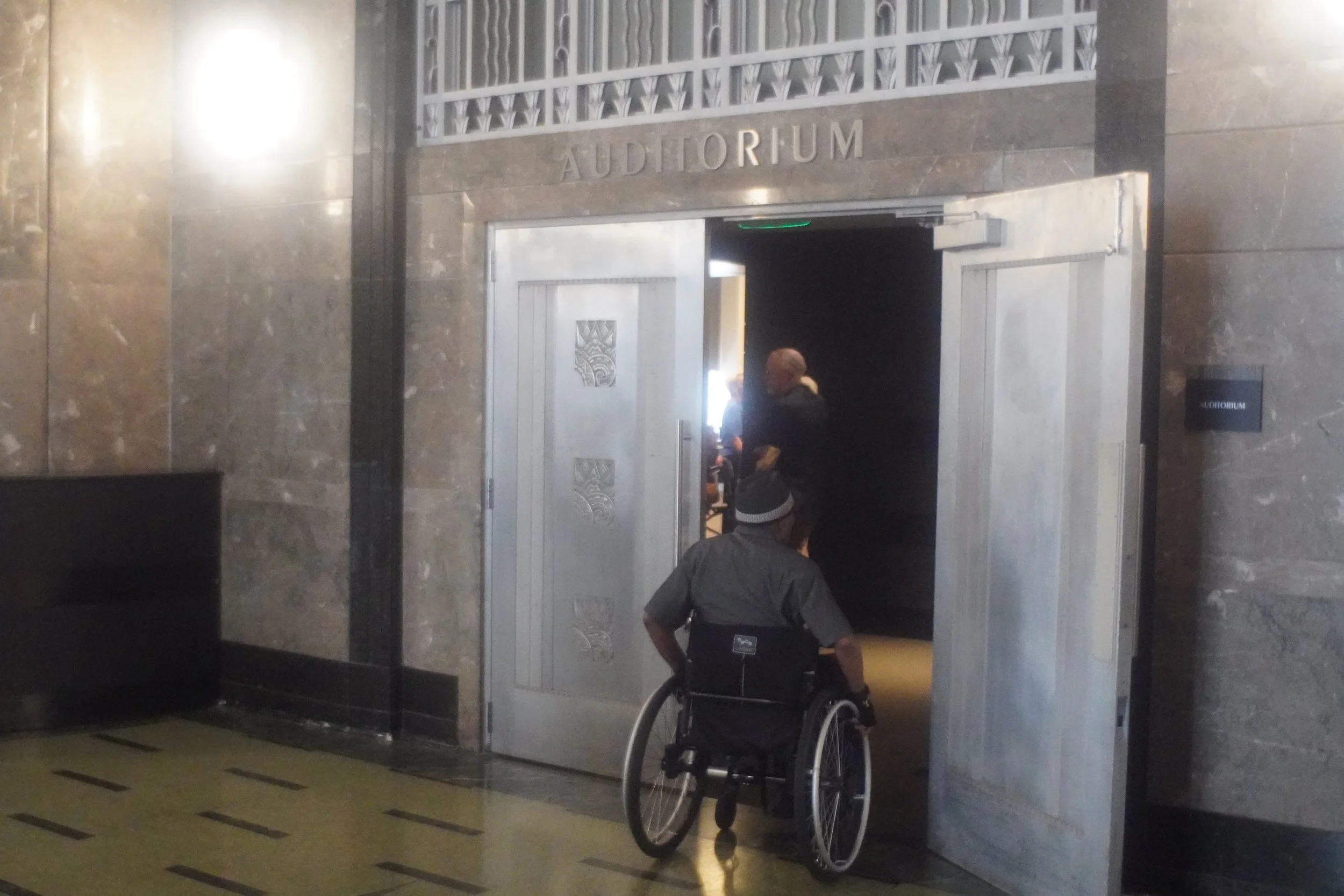 A man in a wheelchair rolls into an auditorium