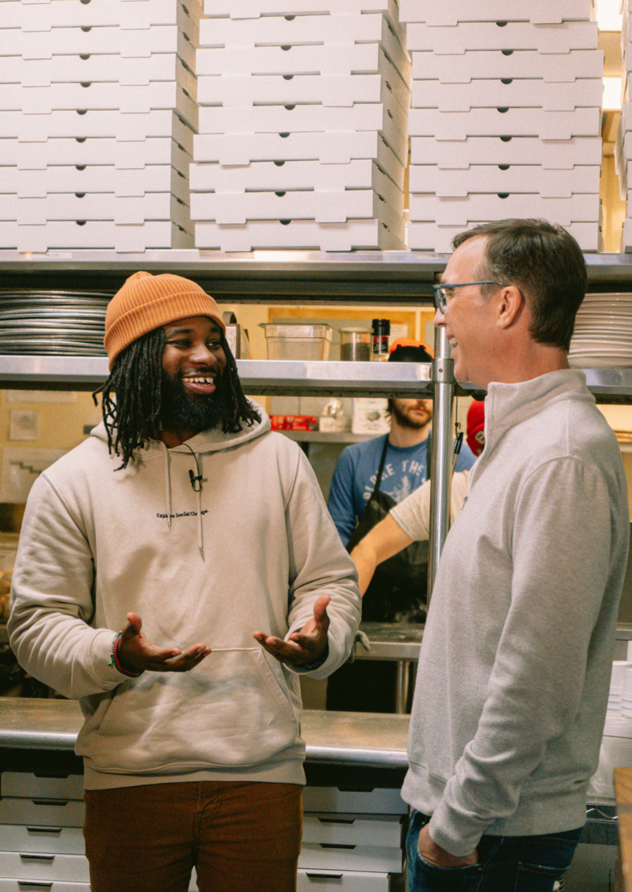 Two men talk in the kitchen of a pizza shop