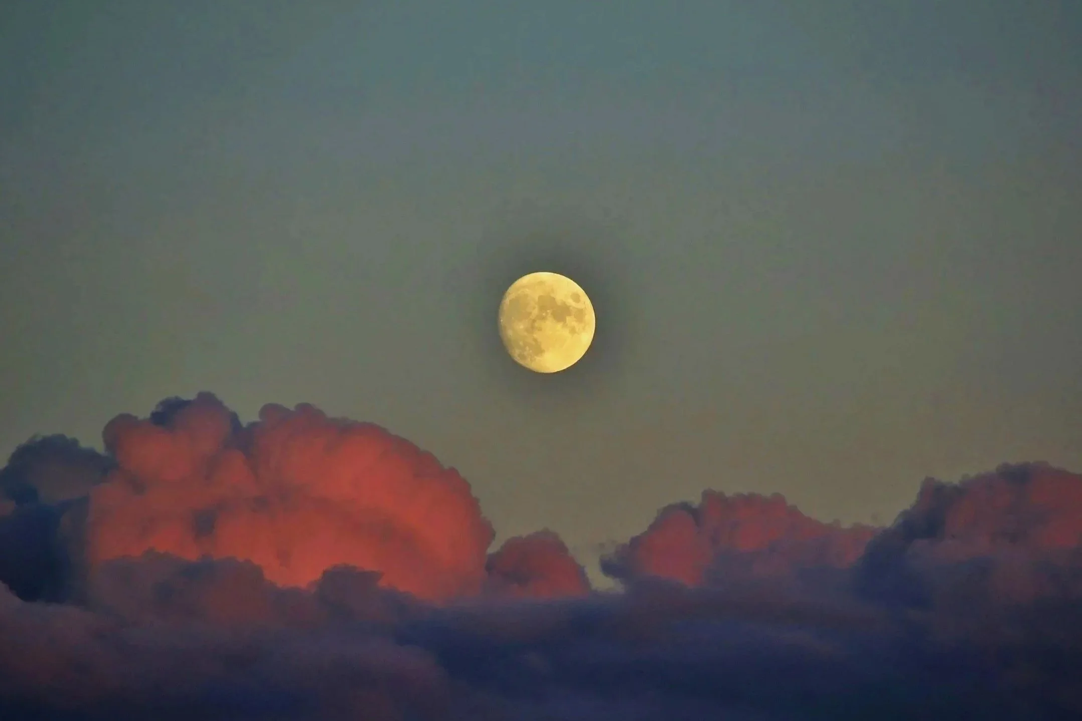 The moon in a partly cloudy sky during sunset or sunrise with pink and purple clouds.