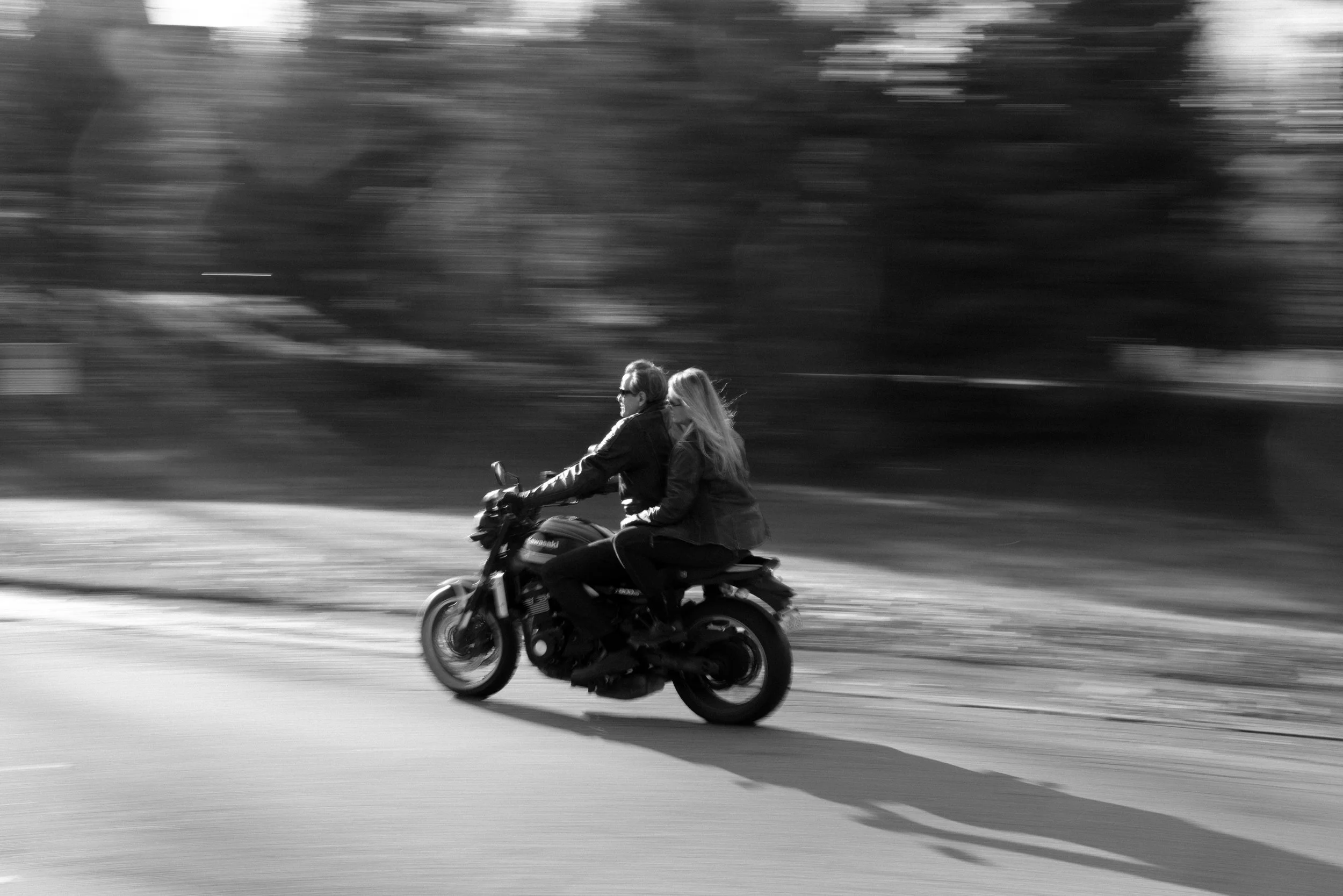 Two women riding a motorcycle on a road with a blurred background in black and white.