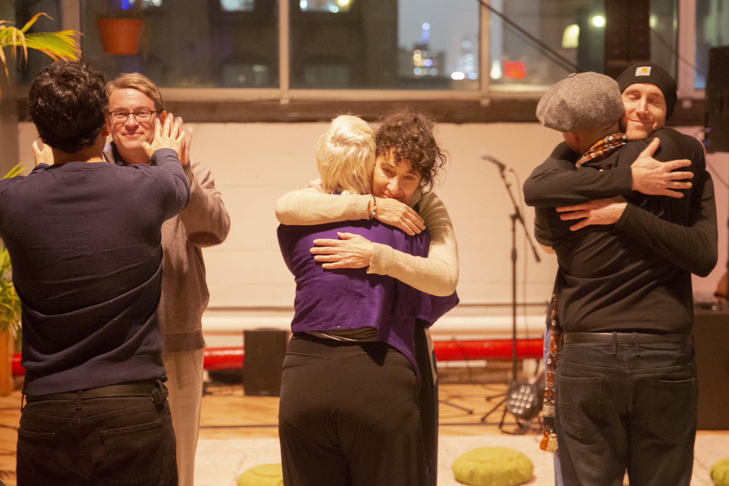 People hugging each other in a warm gathering, with some clapping and smiling.