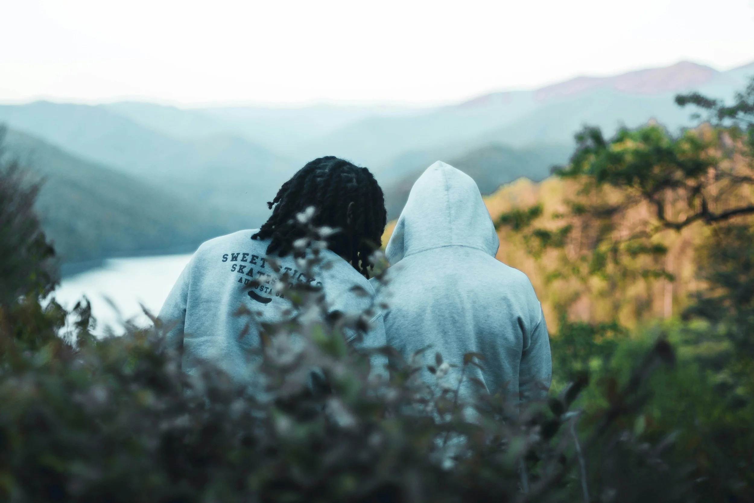 Two friends perched at the top of a mountain, overlooking a lake.