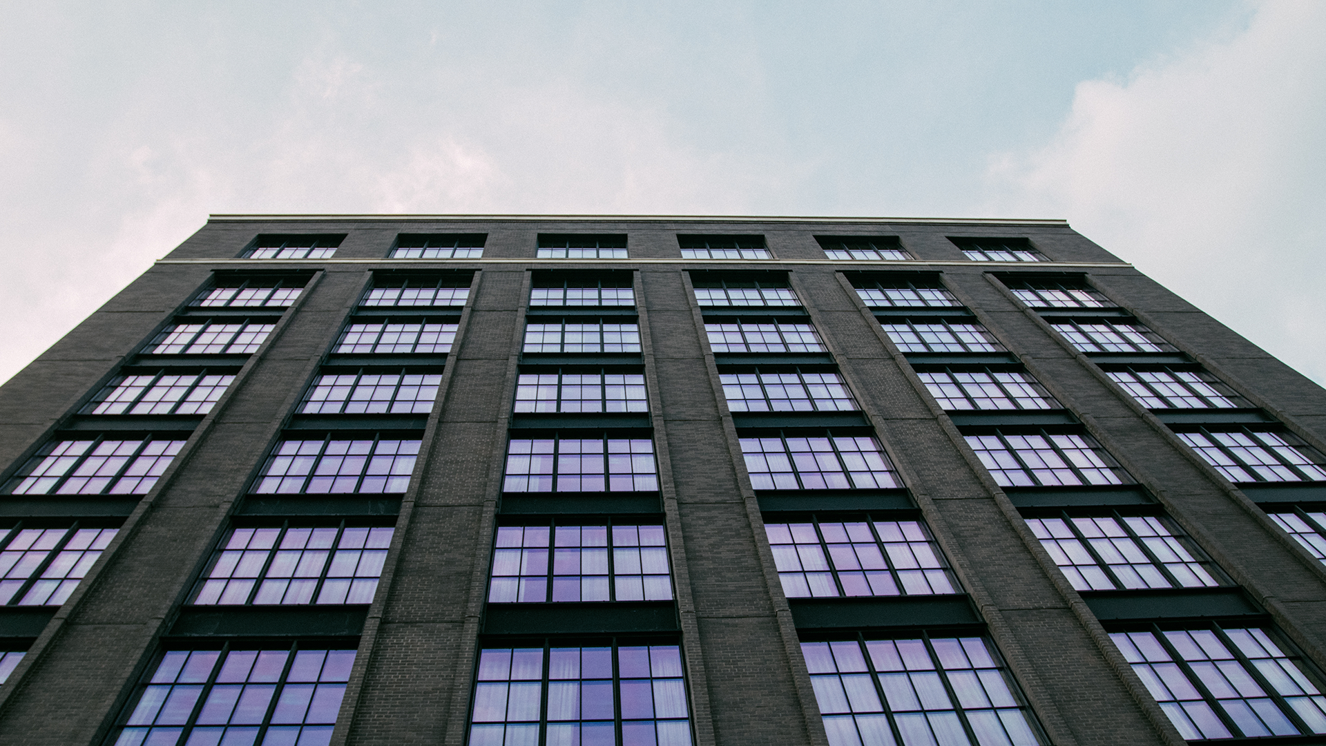 Low-angle view of a tall concrete and glass office building against a partly cloudy sky.