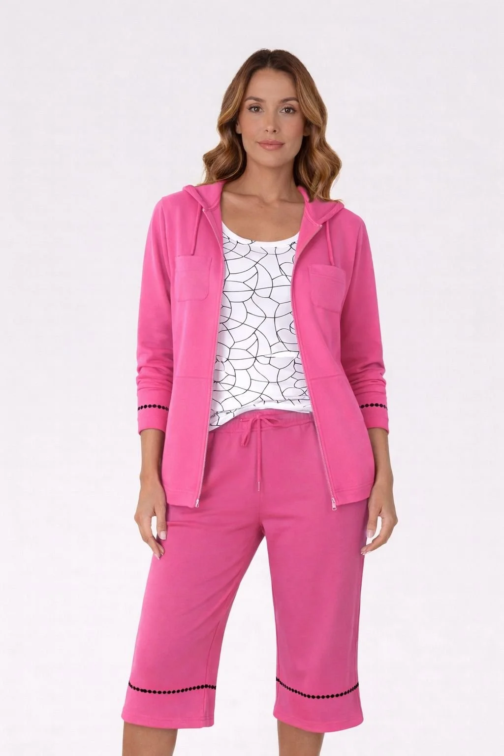 Woman in pink hoodie, matching shorts, and white shirt with black geometric pattern, standing against white background.